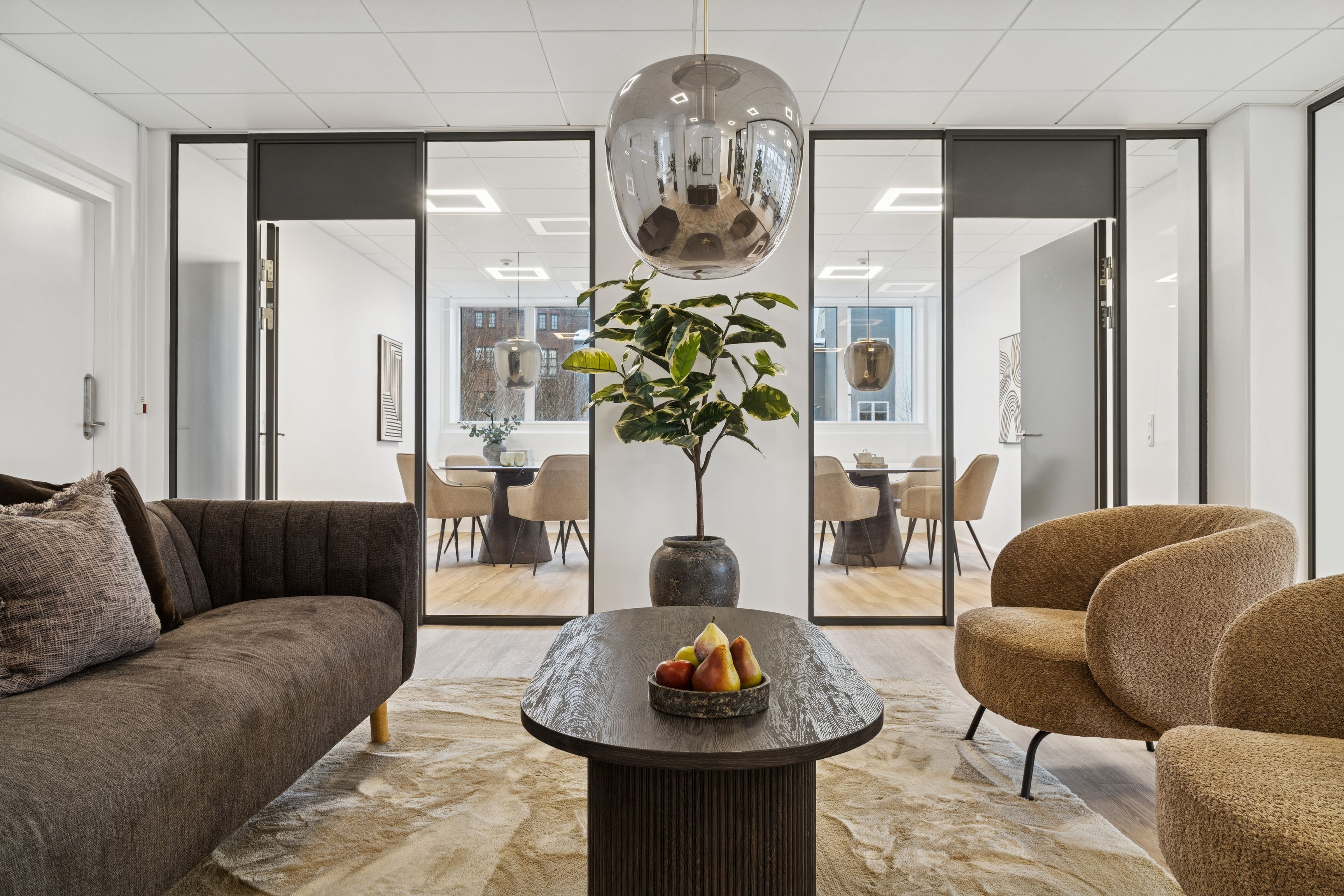 Kontorlokaler med moderne møbler og en plante. Rundt loftslampe, træbord med frugt, og en plante i en stor vase