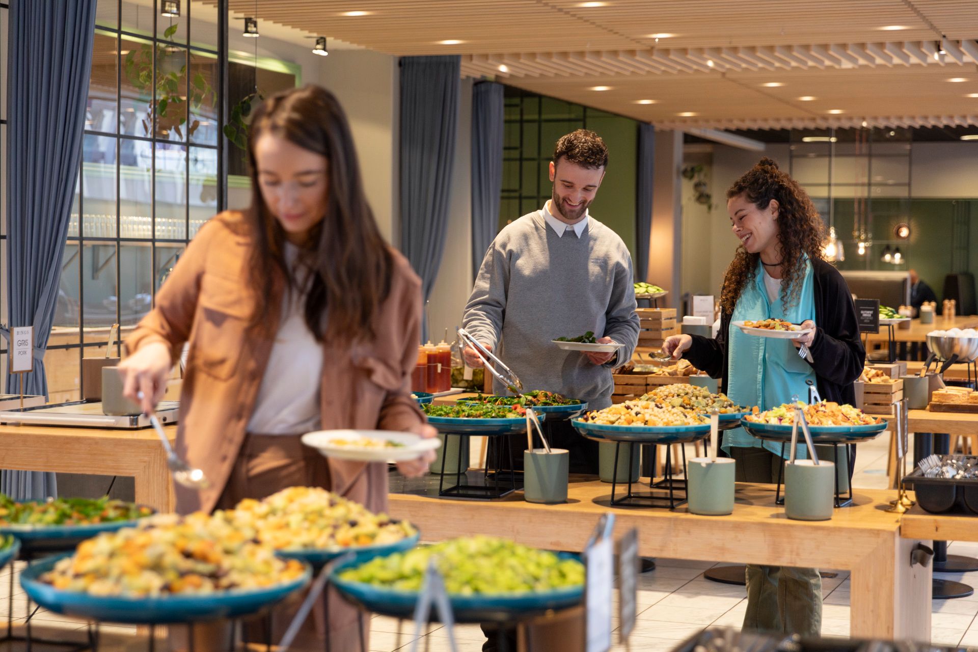 Tre personer i en moderne kontorrestaurant deler mad fra en buffet med økologiske og sunde retter