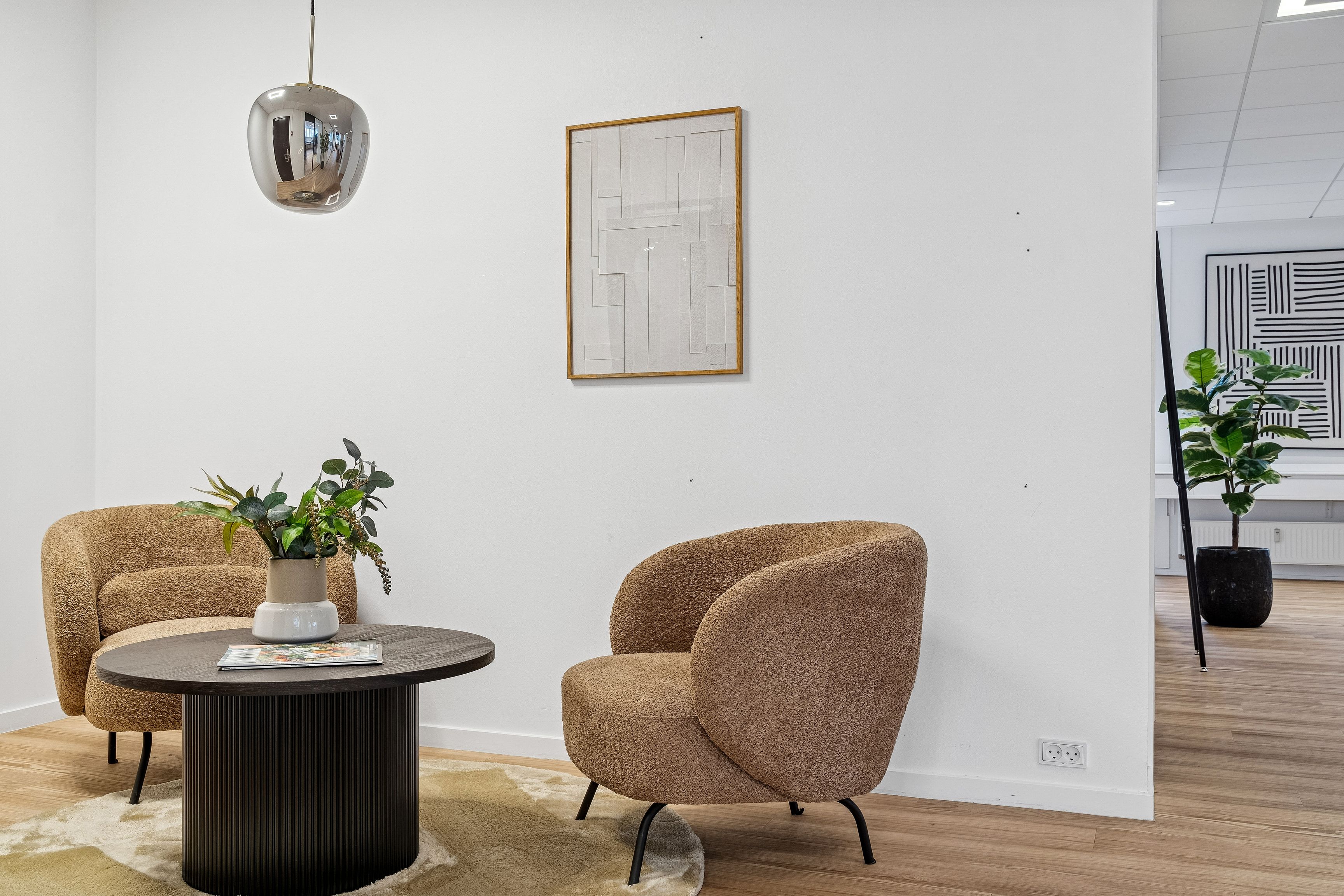Kontor med møbler, gulvtæppe, plante og publikationer på runde bord og billedramme på væg