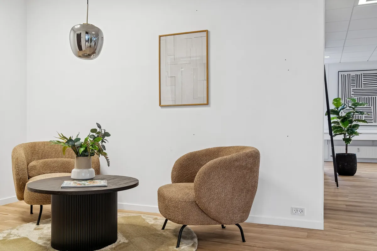Kontor med møbler, gulvtæppe, plante og publikationer på runde bord og billedramme på væg