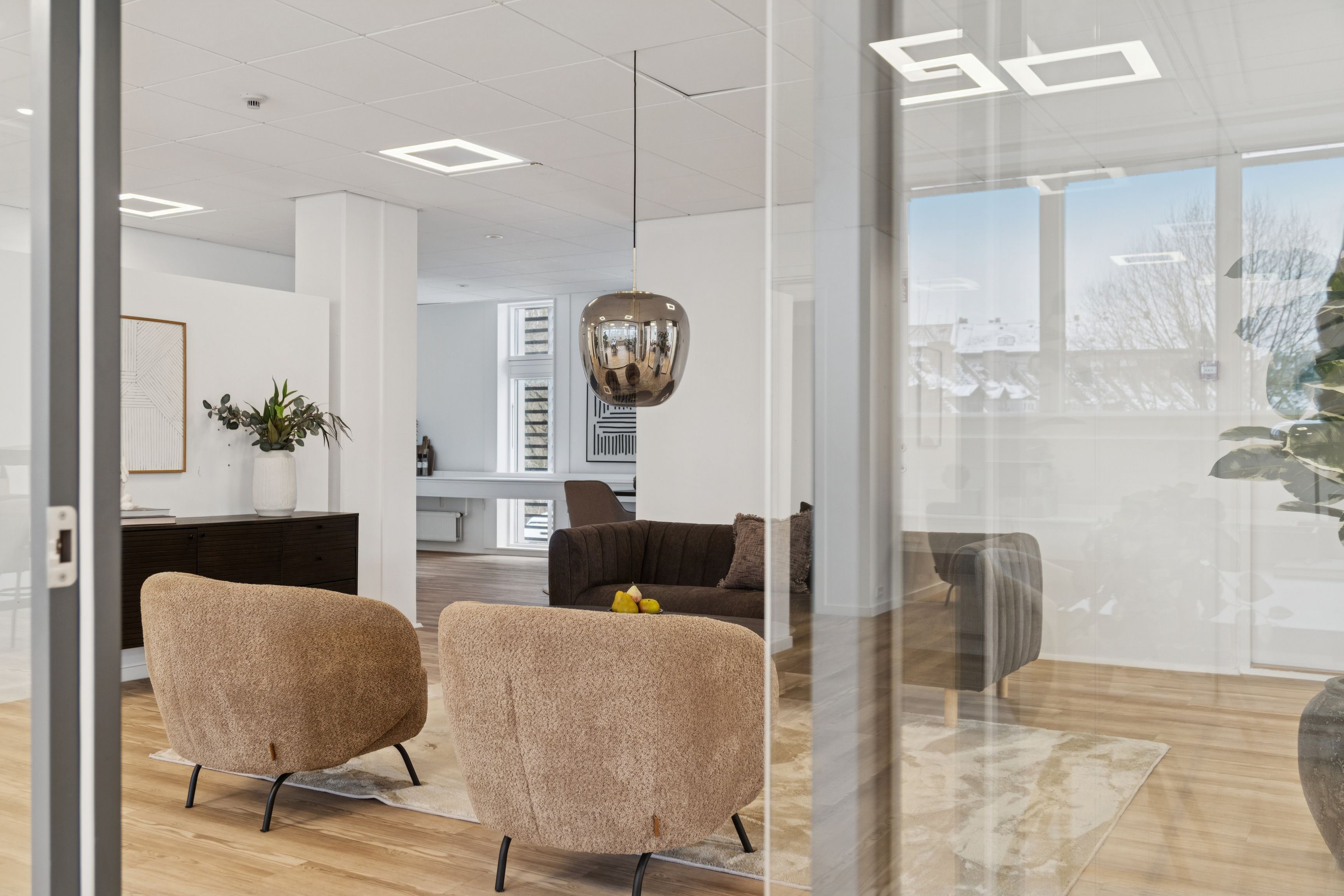 Moderne minimalistisk kontor med høje glasvægge og beige møbler i to hjørner og et brunt sofa med puder