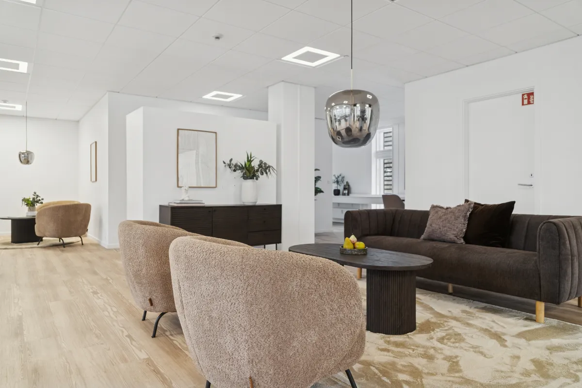 Moderne kontor med højloft og lysegul gulvbelægning, runde beige sæder og mørkebrun sofa med pudsede puder og træbord med frugtskål