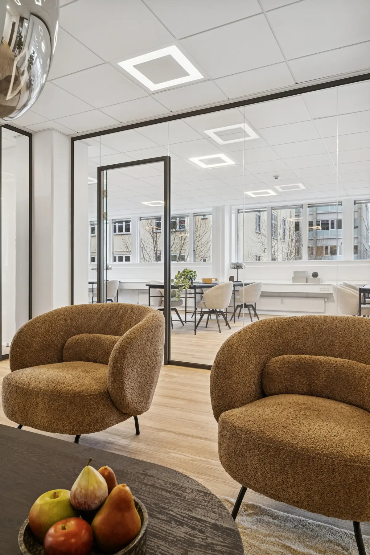 Foto af kontorlokaler med to runde, brune lænestolpe med tæpper og frugtskål på bord og fuldt udstykket mødelokale med stolpe og bord i baggrunden