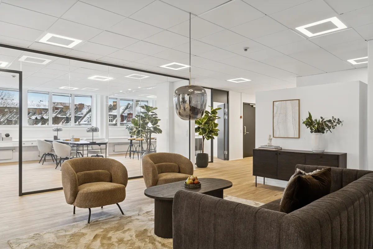 Moderne kontor med højt loft og glasvægge, lyse lamper og elegant møbelplacering, sofa og høj bord i mørk nuance