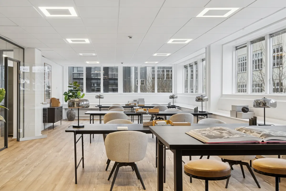 Moderne kontorrum med lyse lofter, høje vinduer og møbler med lave profiler samt lysegulve og beige læderstole