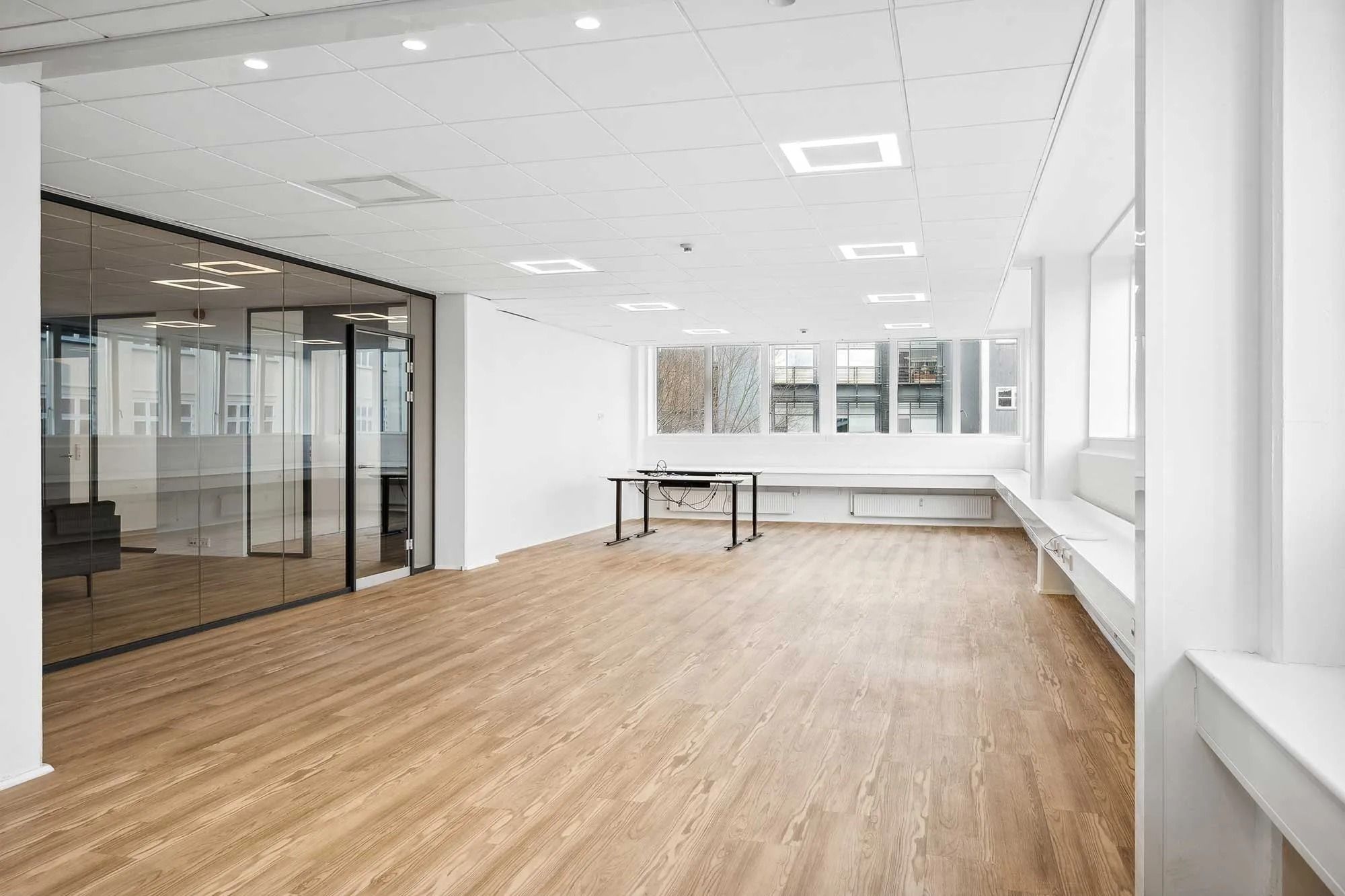 Et rum med højt til loftet og lyse loftsbelægning, gulvbelægning i træ og store vinduer med glas og hvide rammer. To