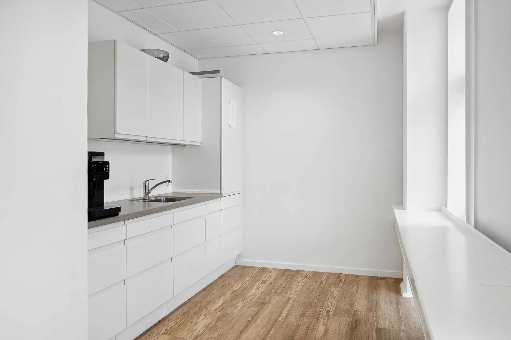 Et moderne køkken med hvide vægge og hvidt loft samt lysegrå gulvbelægning og en enkel spisestue med hvidt bord