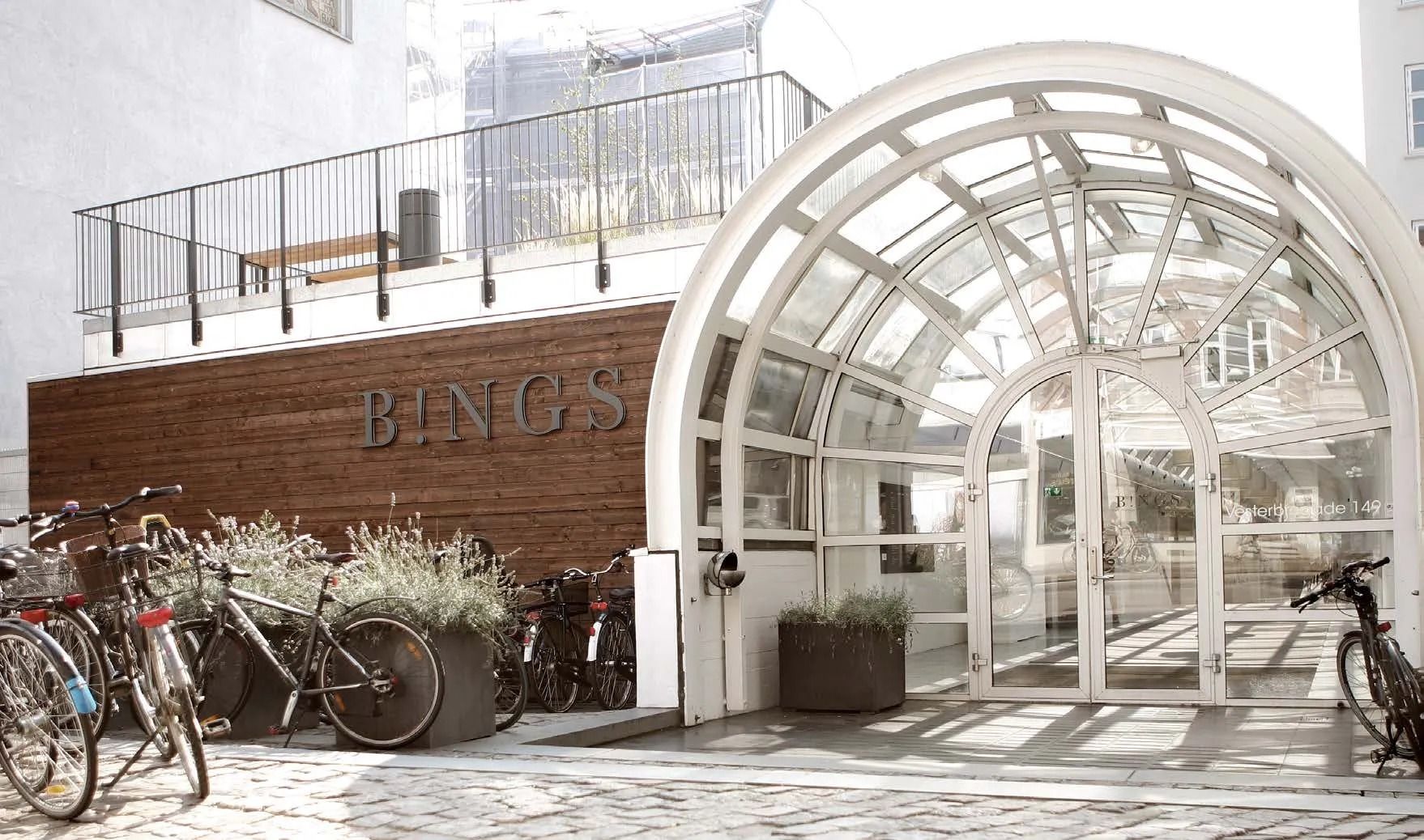 B!NGS kontorbygning med en stor buet glasindgang og en række cykler parkeret udenfor