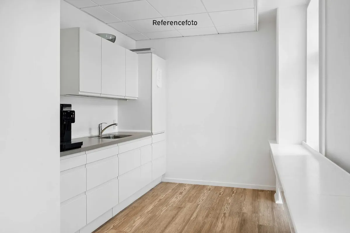 Minimalistisk køkken med hvide vægge og trægulv, køkkenskabe, køleskab, sink og en kaffemaskine i sort og sølv