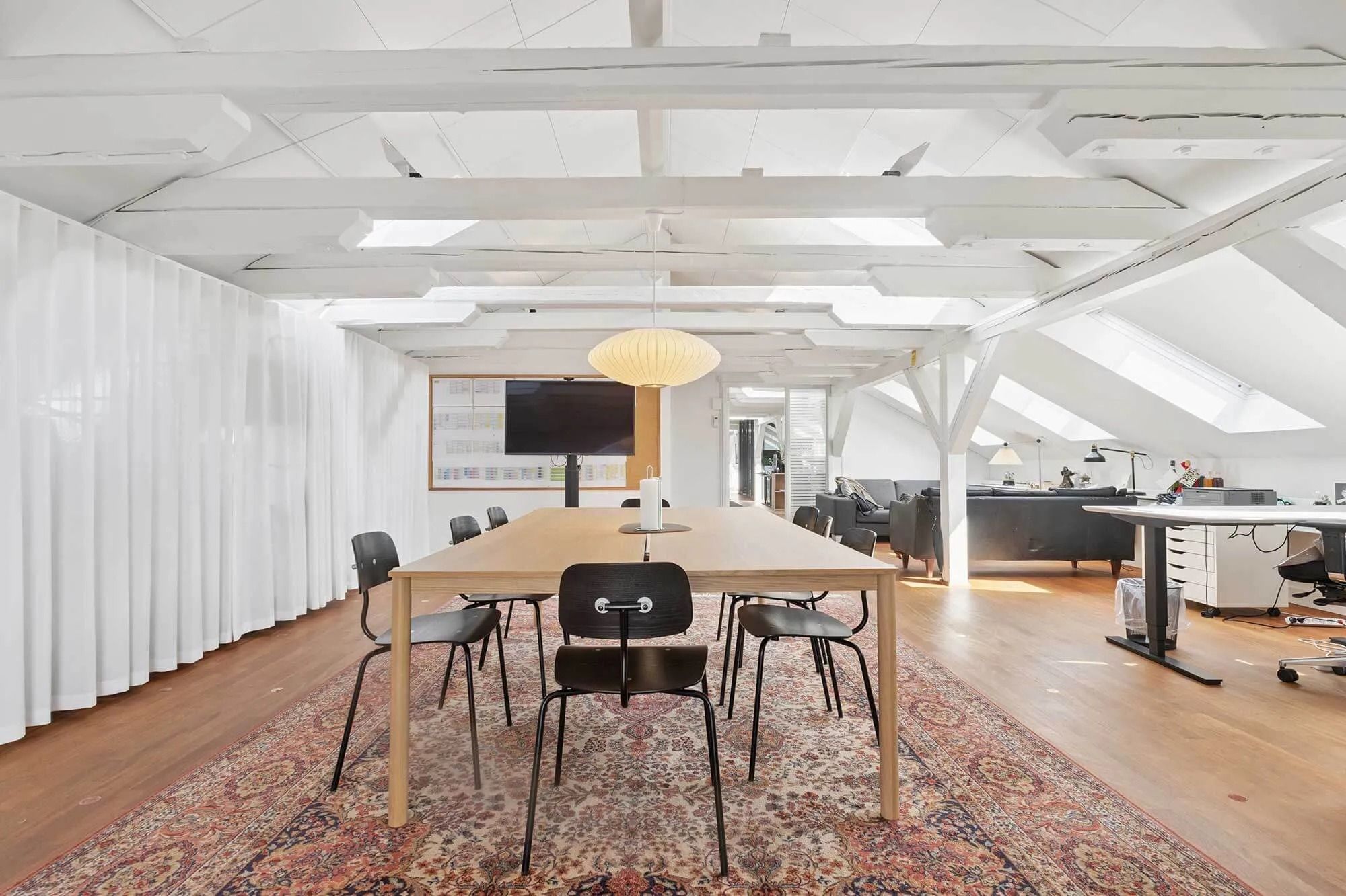 Lyst kontor med møbler og tekstiler i lyse farver og store vinduer, hvor solen skinner ind