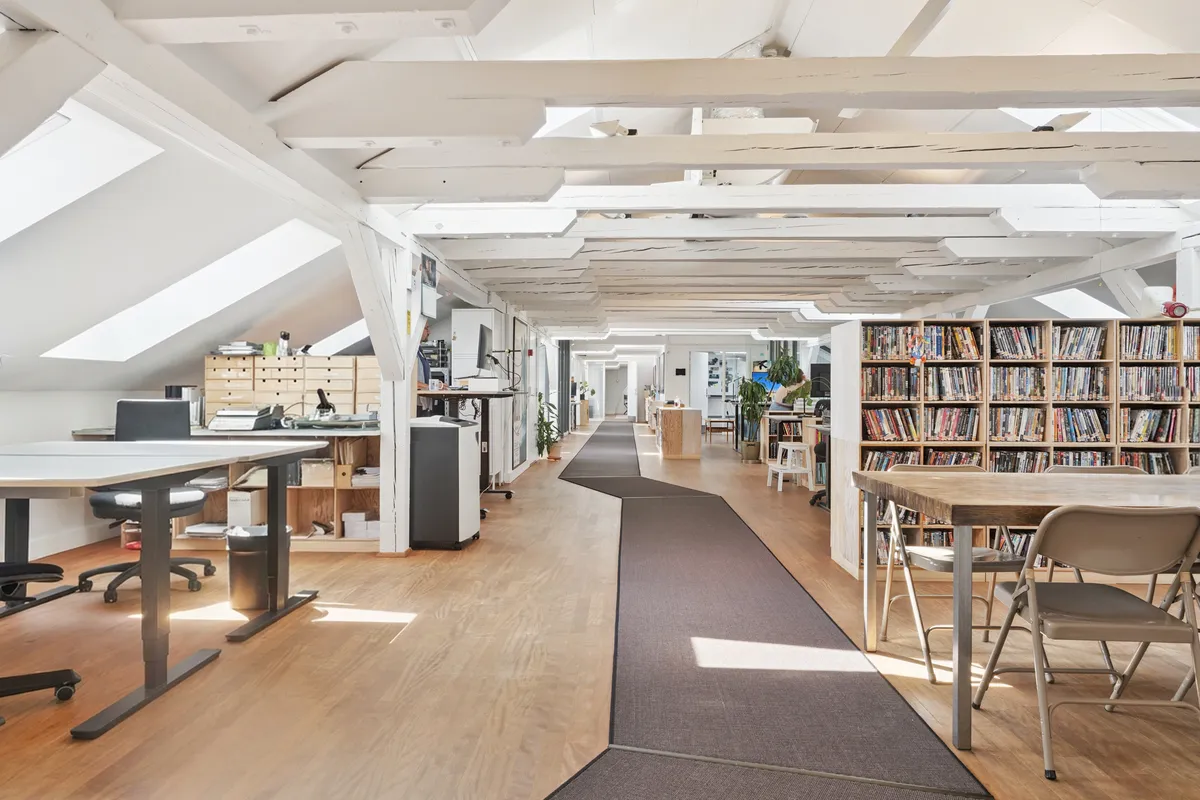 Et lyst kontor med højloft og masser af vinduer. Her er flere borde og stole samt en lang række hylder med dvd’er.