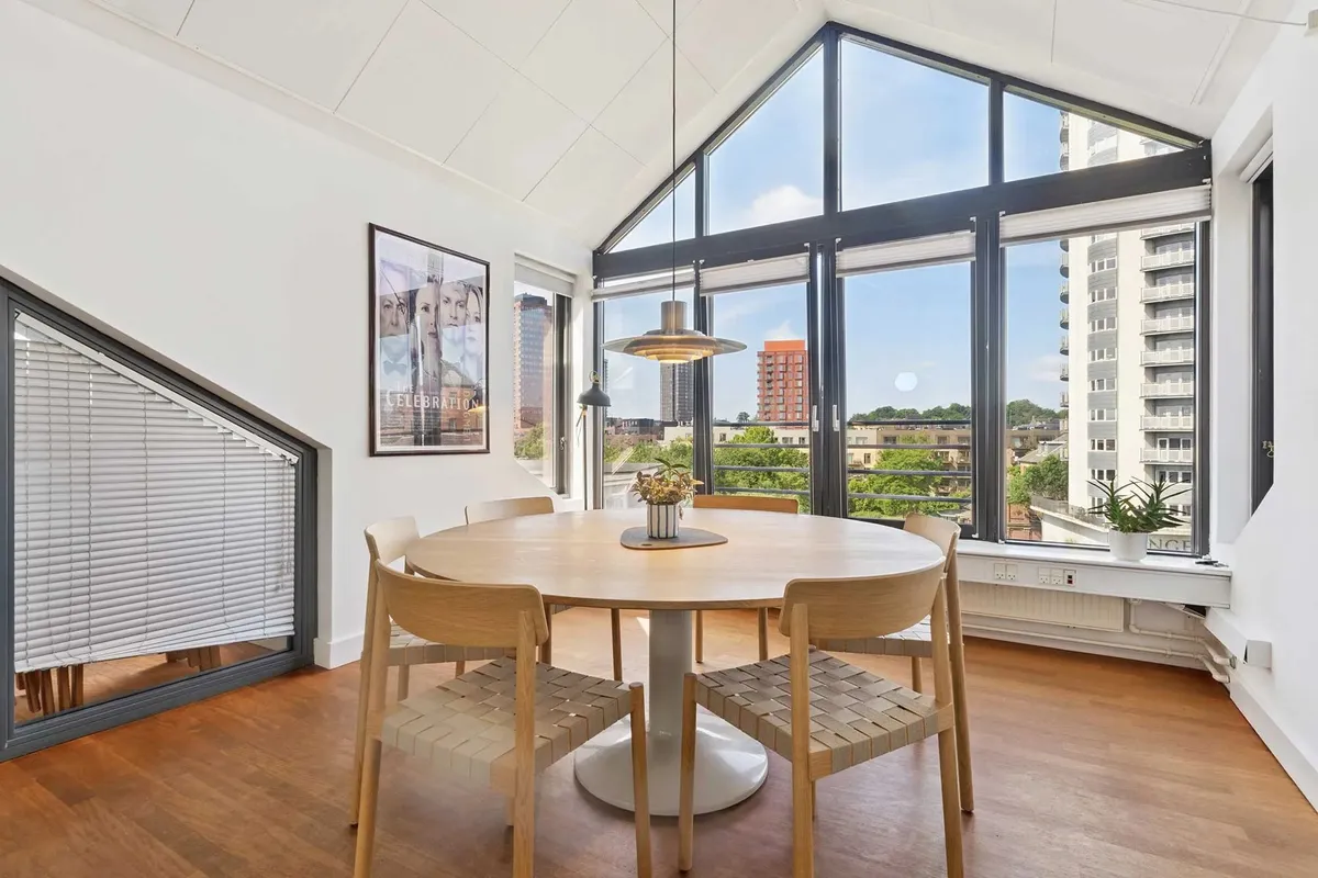 En lyse stue med runde træbord og stole samt plante i hvidt keramikpot og lysegardiner