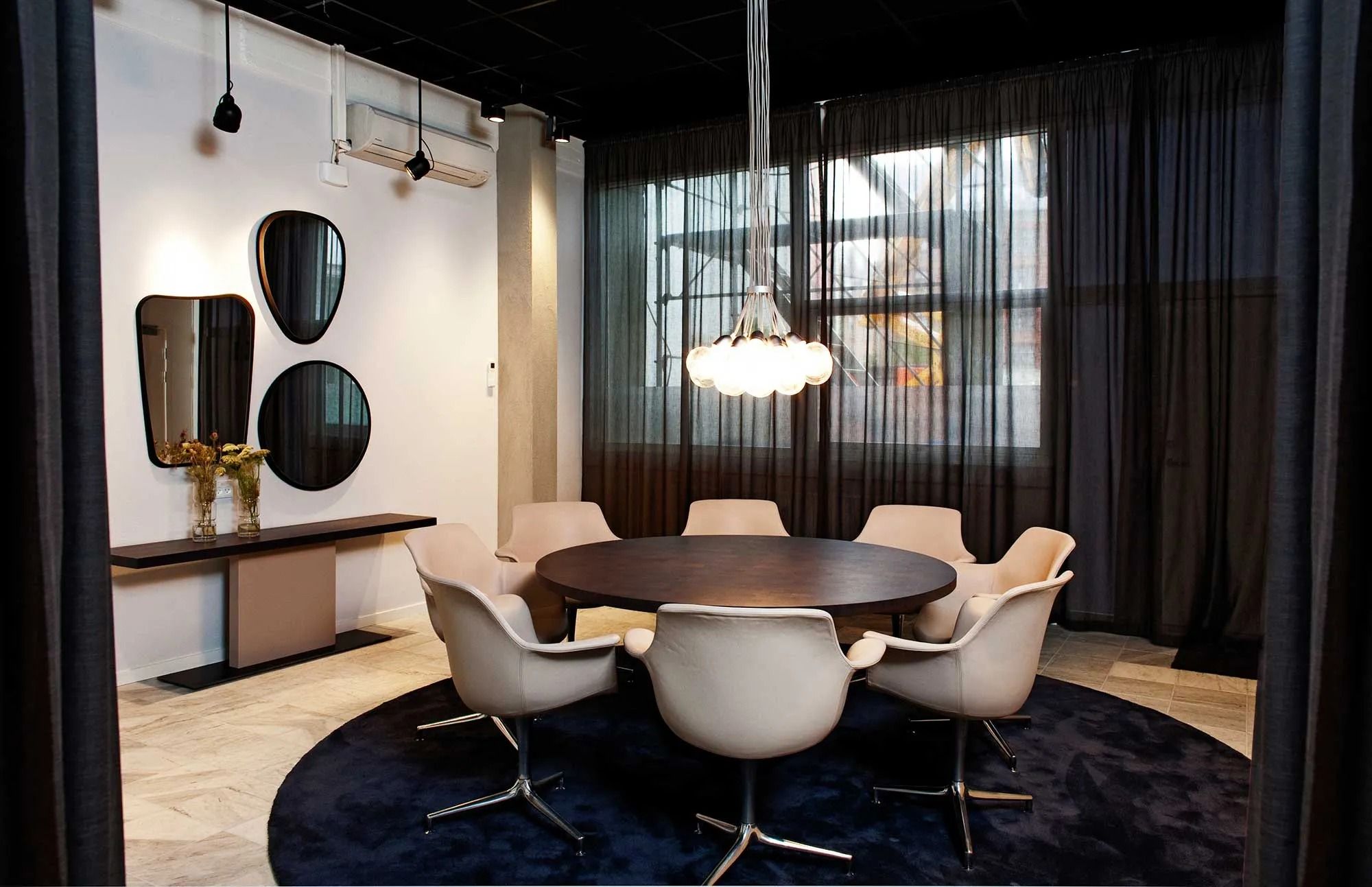 Runde bord med otte stole omkring samt tre spejl med lysekroner. Møbler og tekstiler er pænt lyse og møblerne er placeret på