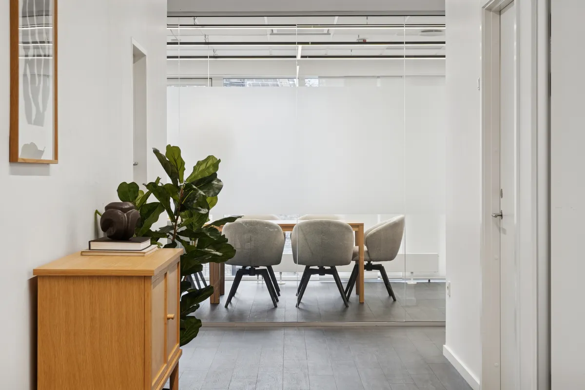 Kontor med højt glasloft og højt gulv. Bord og stole i glas og træ. Plante og skulpturer på et bord. Alle kontorer er hvide.