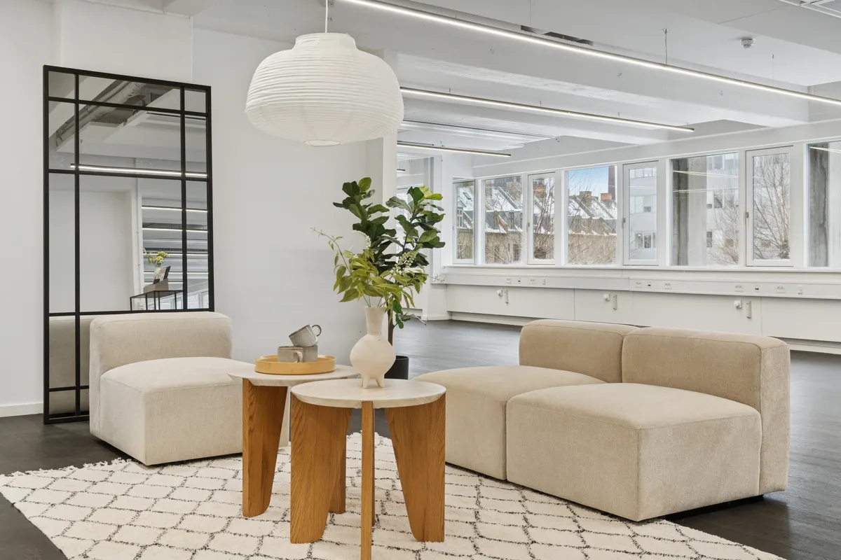 Kontor til leje på Vesterbrogade 149 med lyse vinduer og lyse loftsbånd. Møbler med lyse farver og en plante i et hvidt fad. Et hvidt sengehoved reflekteres i et spejl