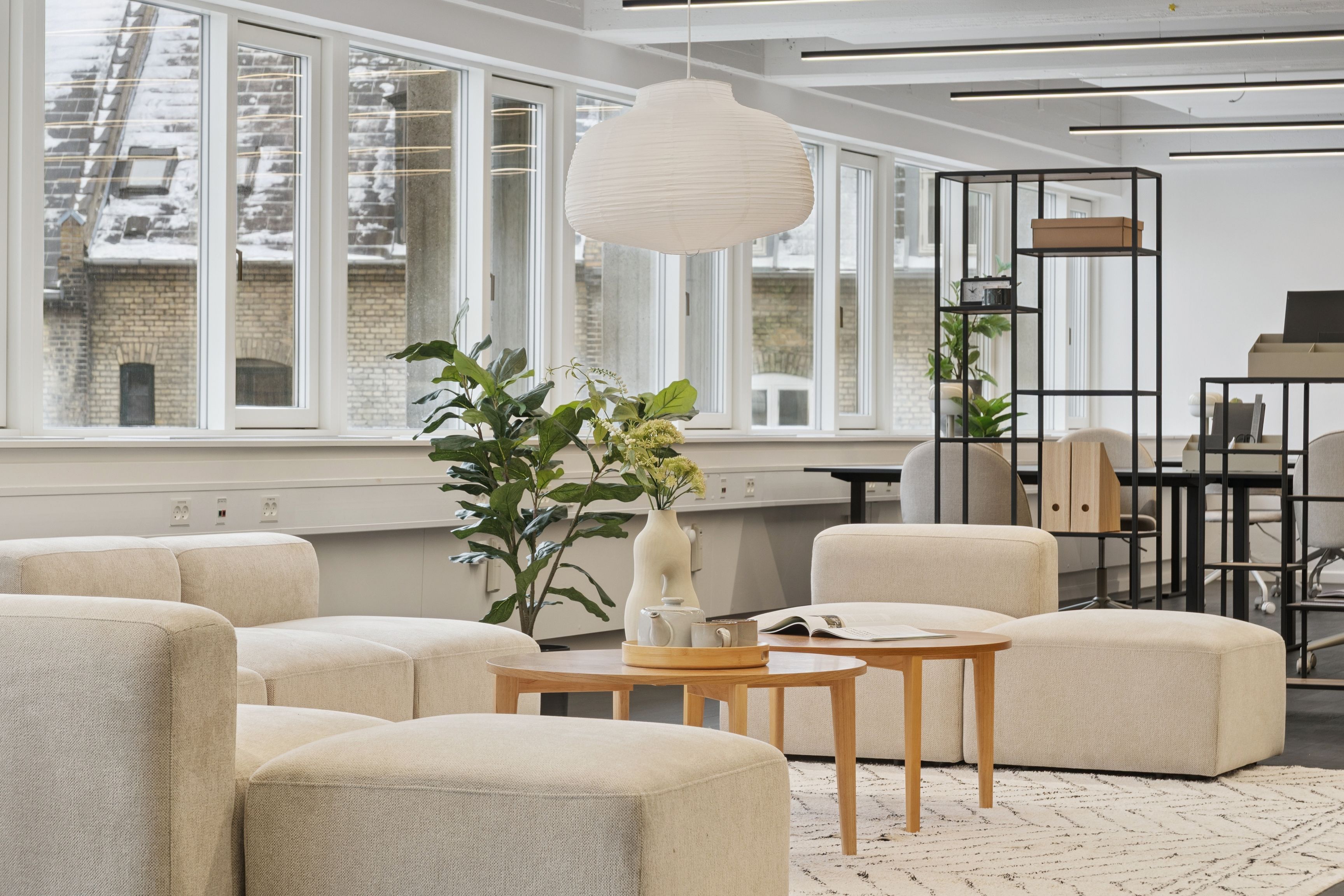 Kontor med loftsvinduer og lys lysekroner, træborde, hvide møbler og lysegulvtæppe samt plante og blomster i en vase