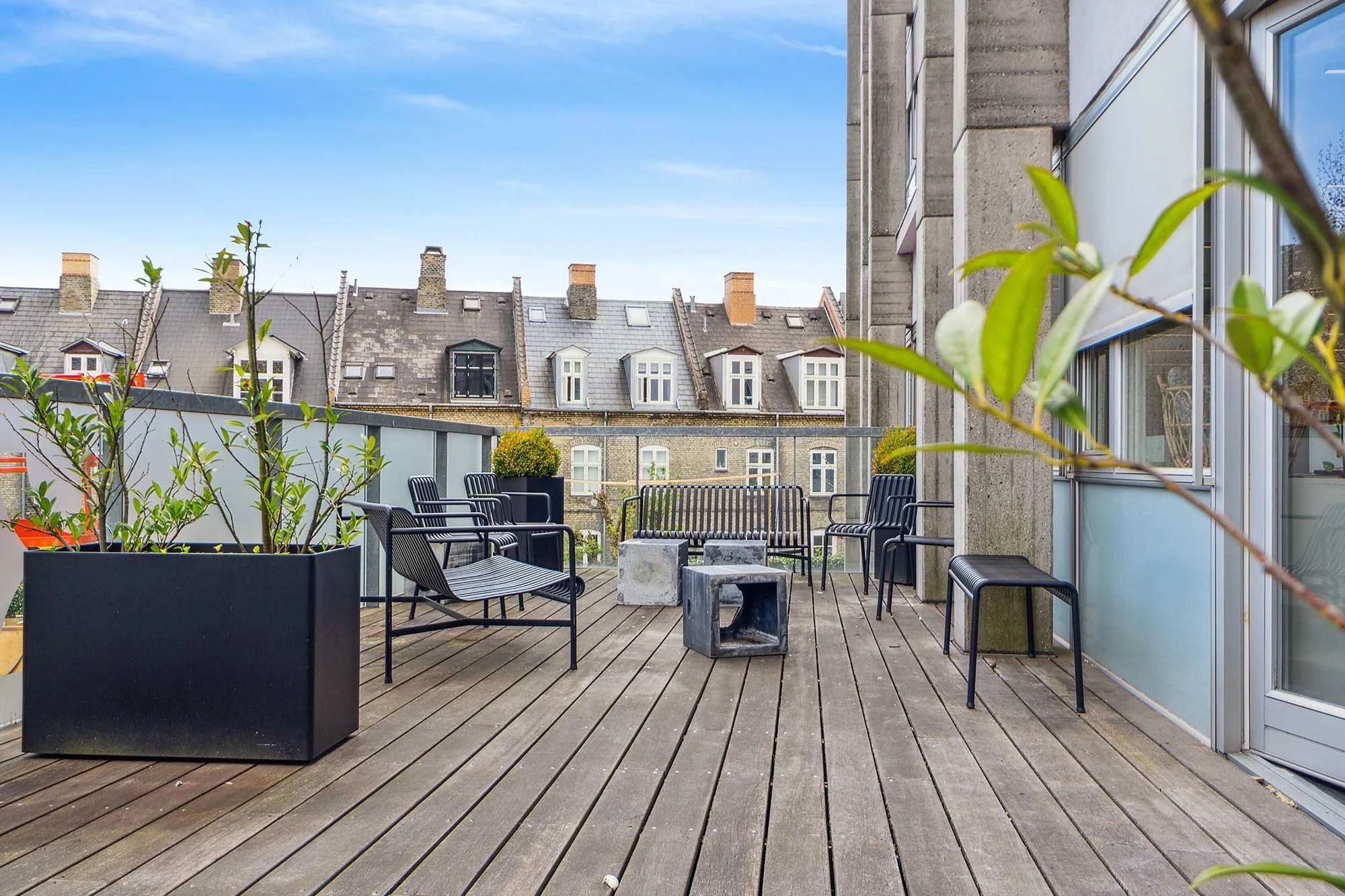 Terrasse med møbler, plantepotter og en smuk udsigt over bygningerne og røgkammeret