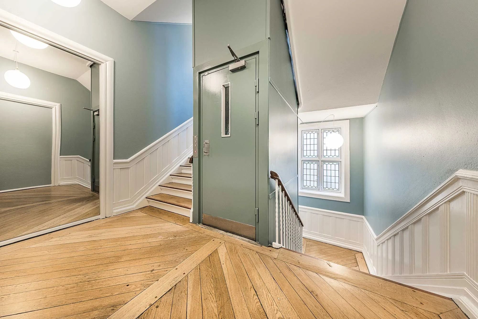 Køkken med højloft, massivt trægulv og lyserøde vægge samt lysekroner og vindue med udsigt til gårdhave