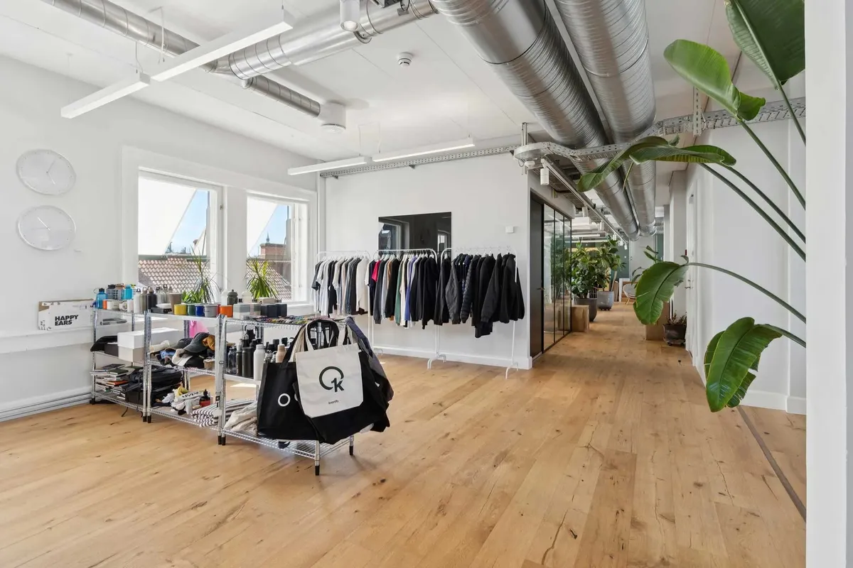 Inde i en moderniseret kontorbygning med højloftede rum, et rack med tøj og flere store planter