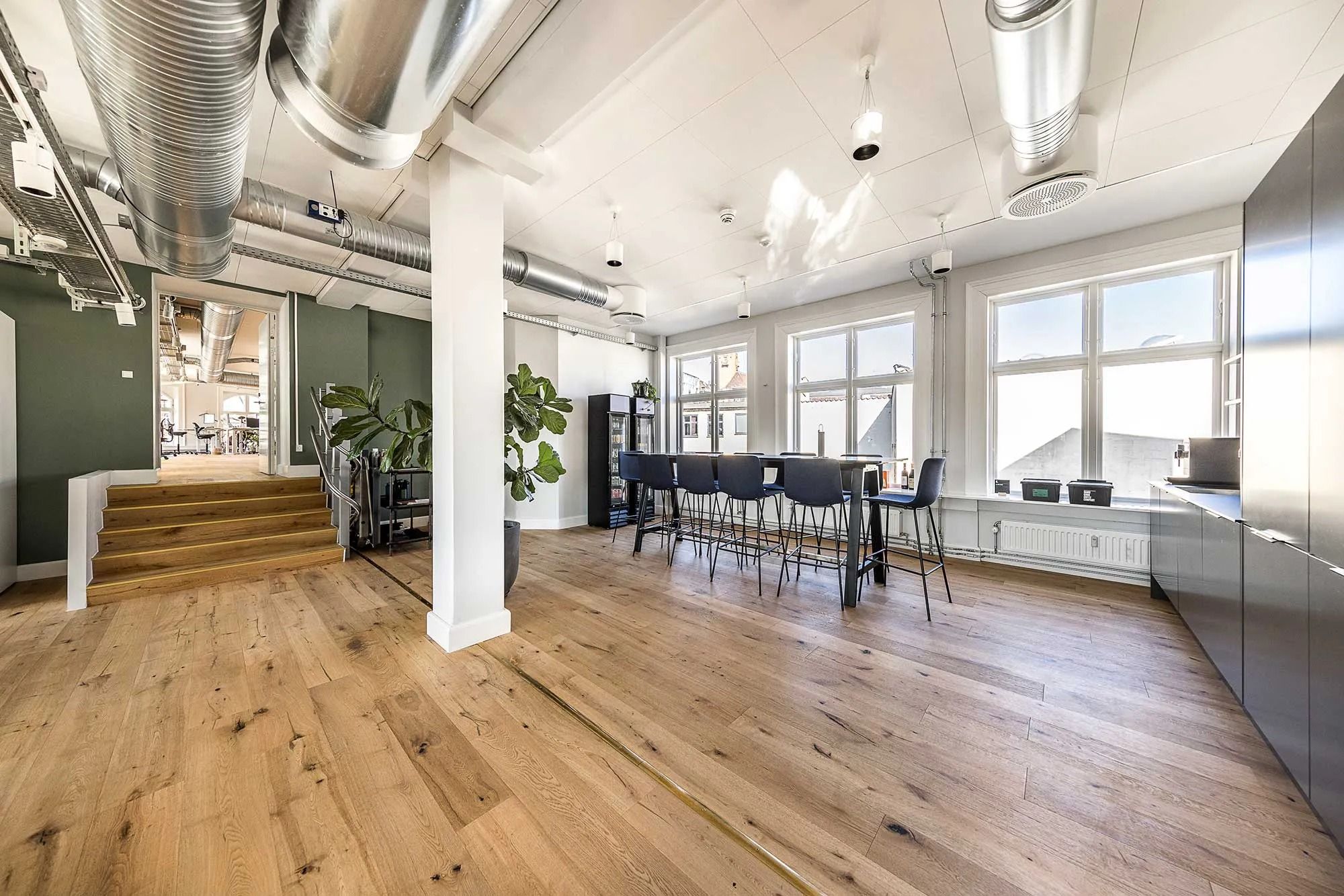 Modernt kontor med højloft og massivt trægulv, med møbler og indretning til kollektivt arbejde og møder