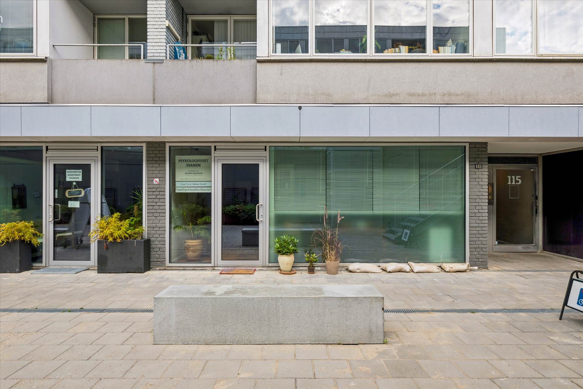 Psykologpraksis med plantager, vinduer og sandposer foran døre og indgangsområde til lejlighedsbygning.