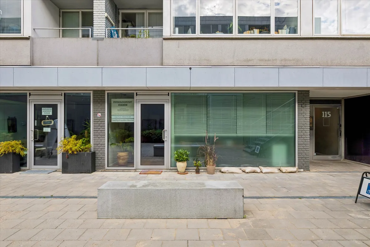 Psykologpraksis med plantager, vinduer og sandposer foran døre og indgangsområde til lejlighedsbygning.