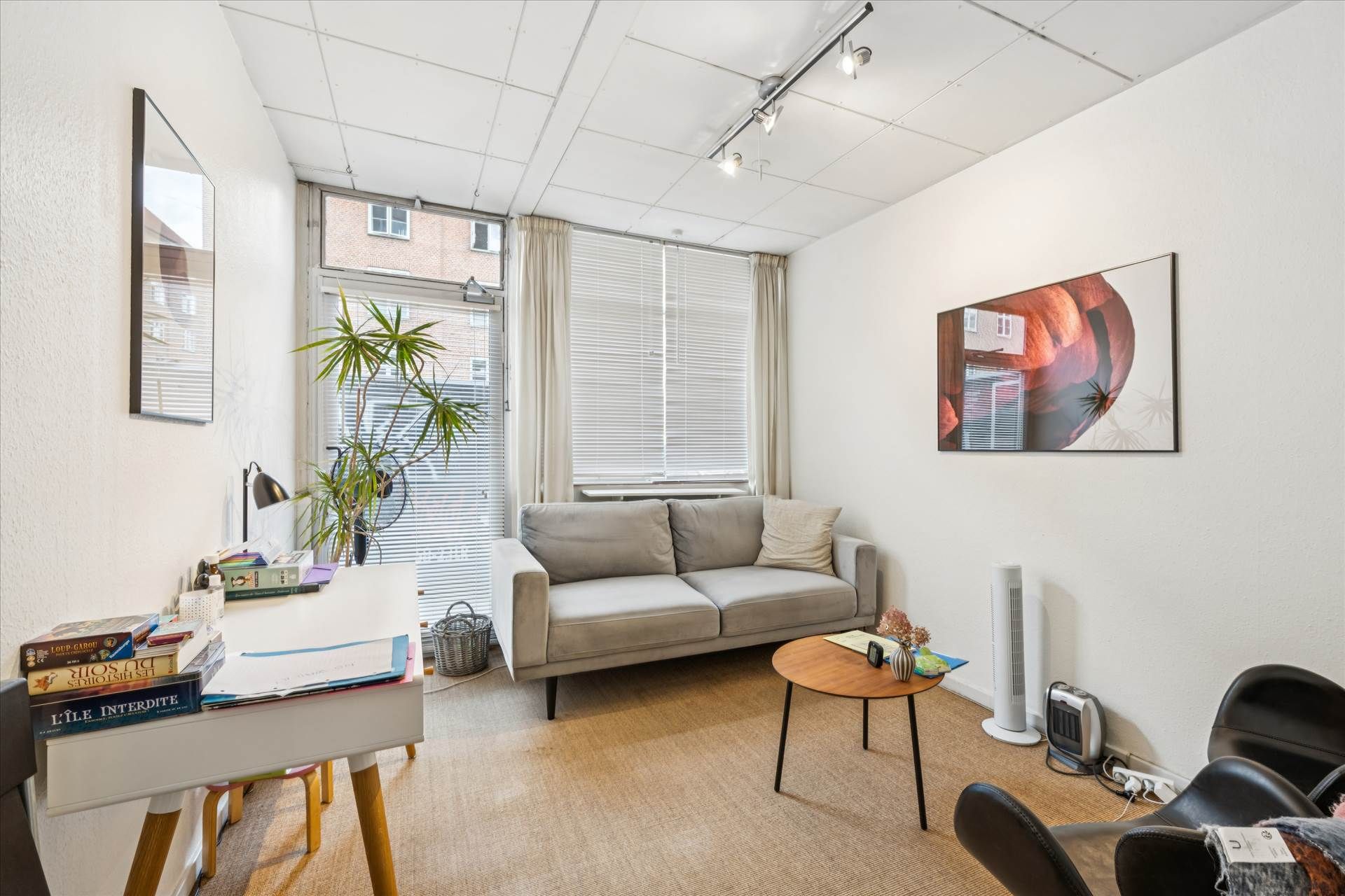 En stue med læderstole, et skrivebord, et sovesofa og et kunstværk. En plante og en ventilator står på gulvet.