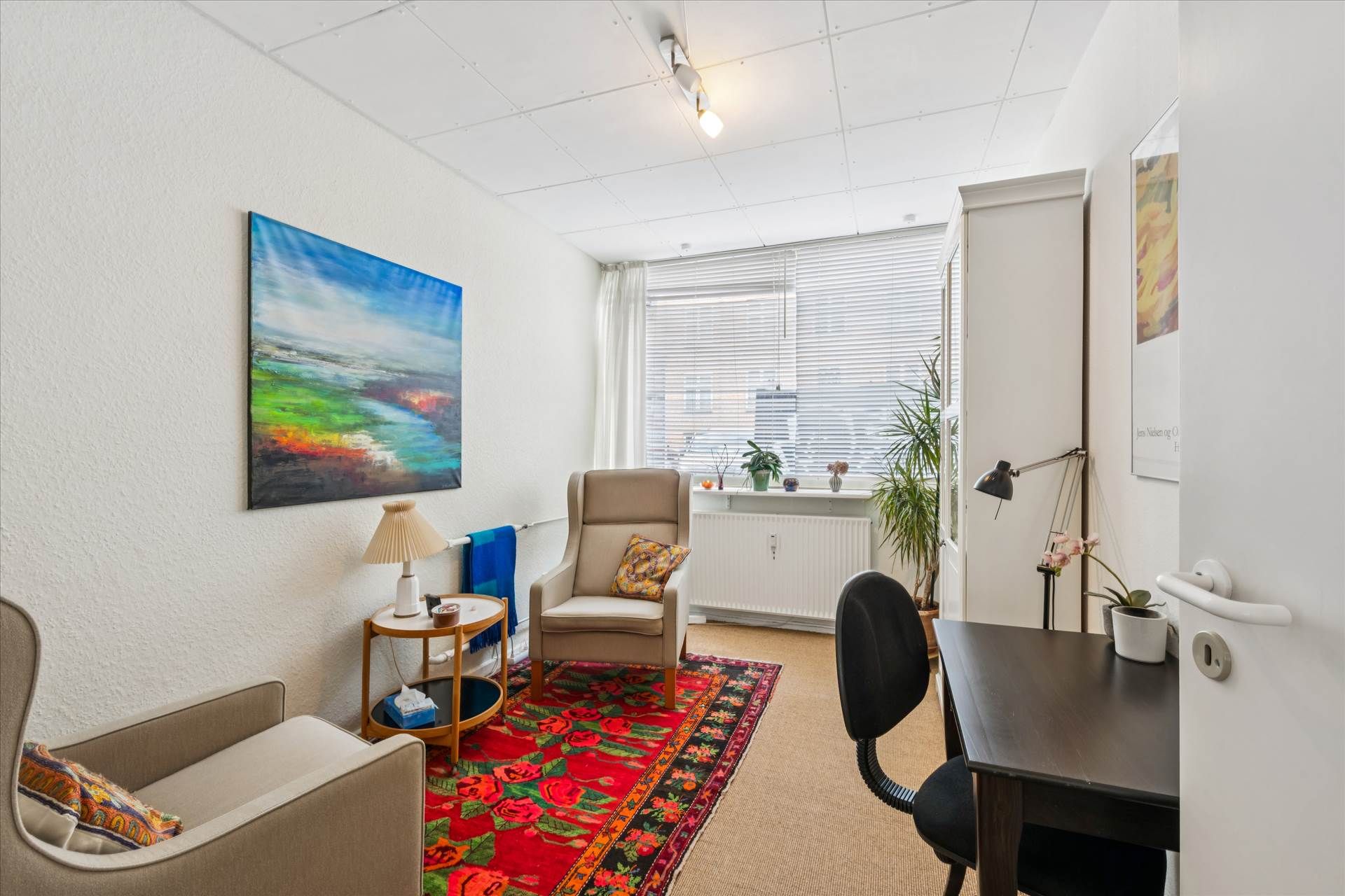 Et studie med en sofa, en lampe og en røgfarvet tæppe på gulvet og et bord med en blomst i en potte på det