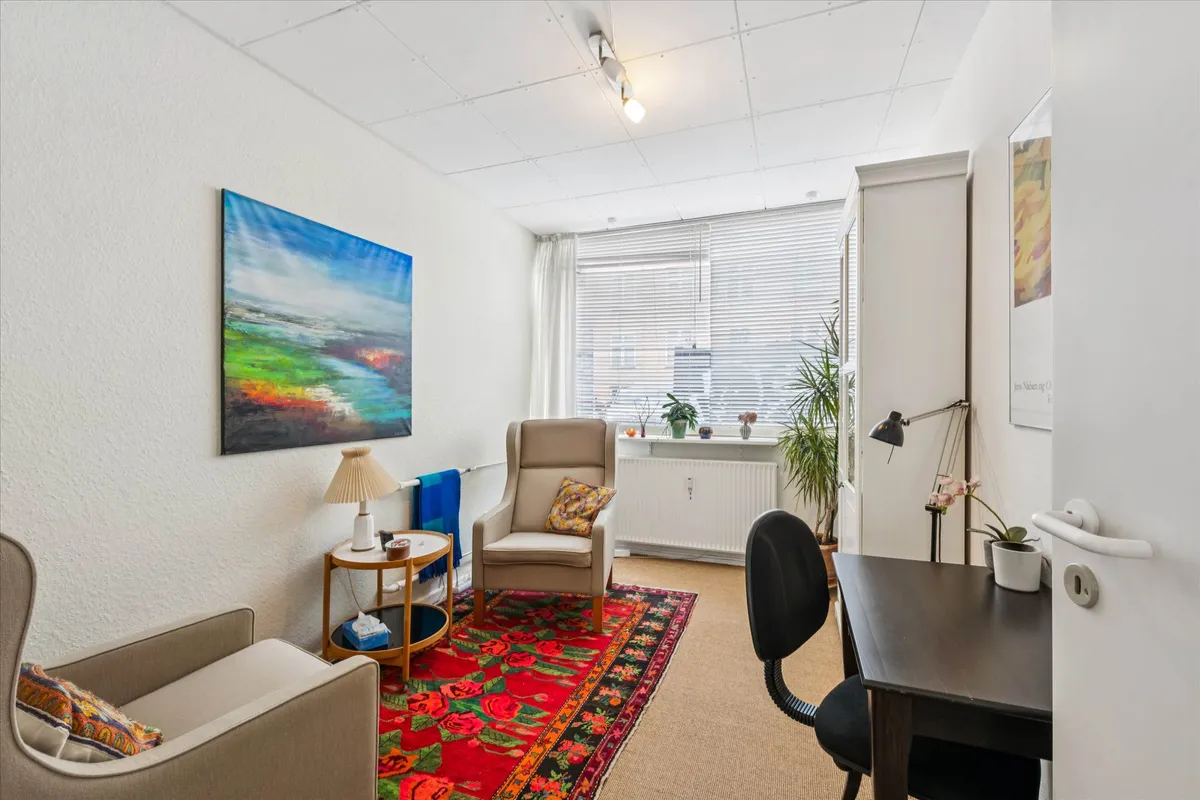 Et studie med en sofa, en lampe og en røgfarvet tæppe på gulvet og et bord med en blomst i en potte på det