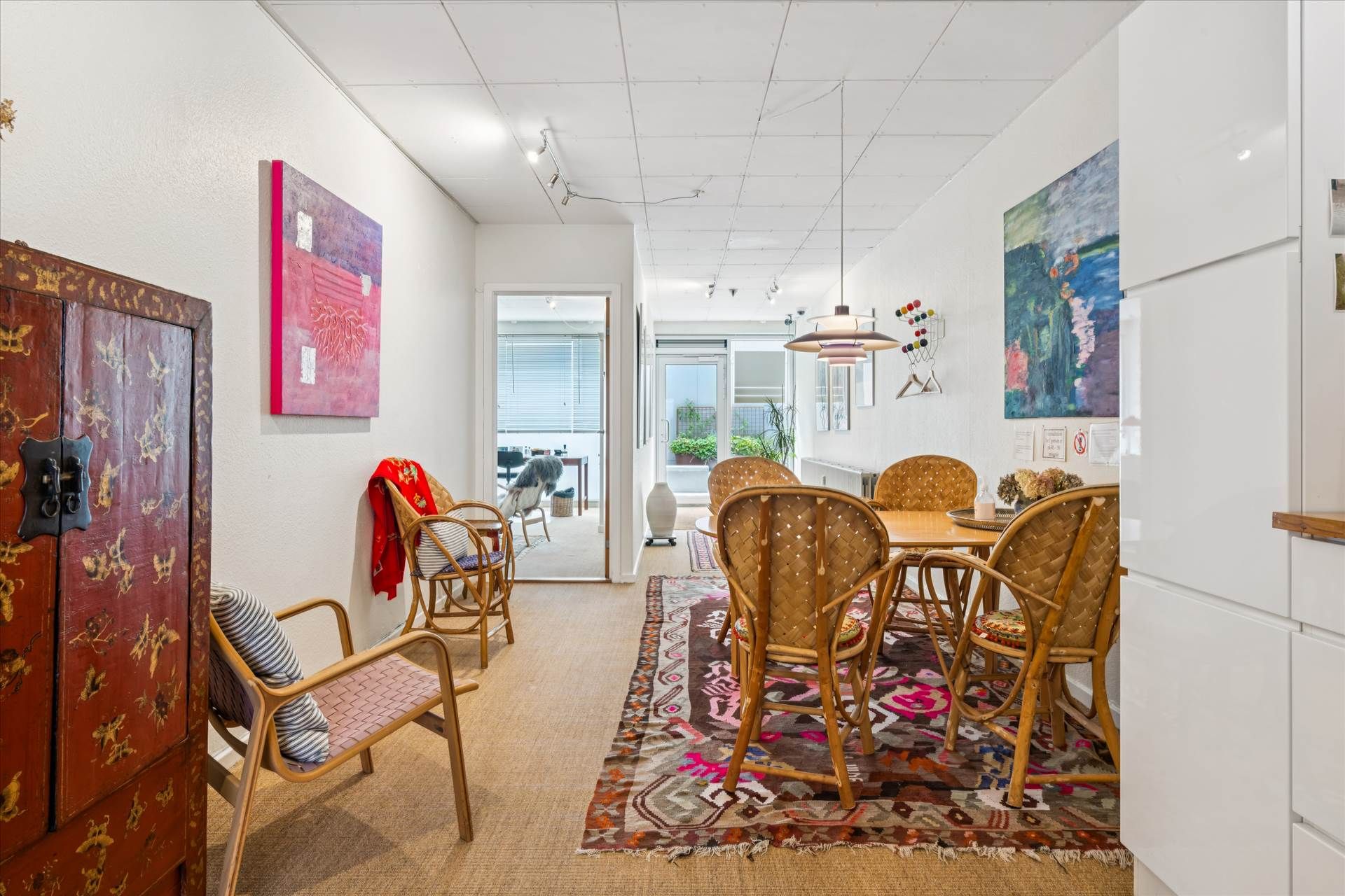 Indretningsfuld stue med lyse vægge, orientalsk tæppe, lyse træstole, lysekroner og moderne malerier