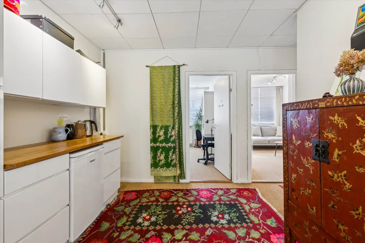 Køkken med hvide skabe og træbordplade, tebrygger, kaffemaskine og en stor orientalsk tæppe på gulvet