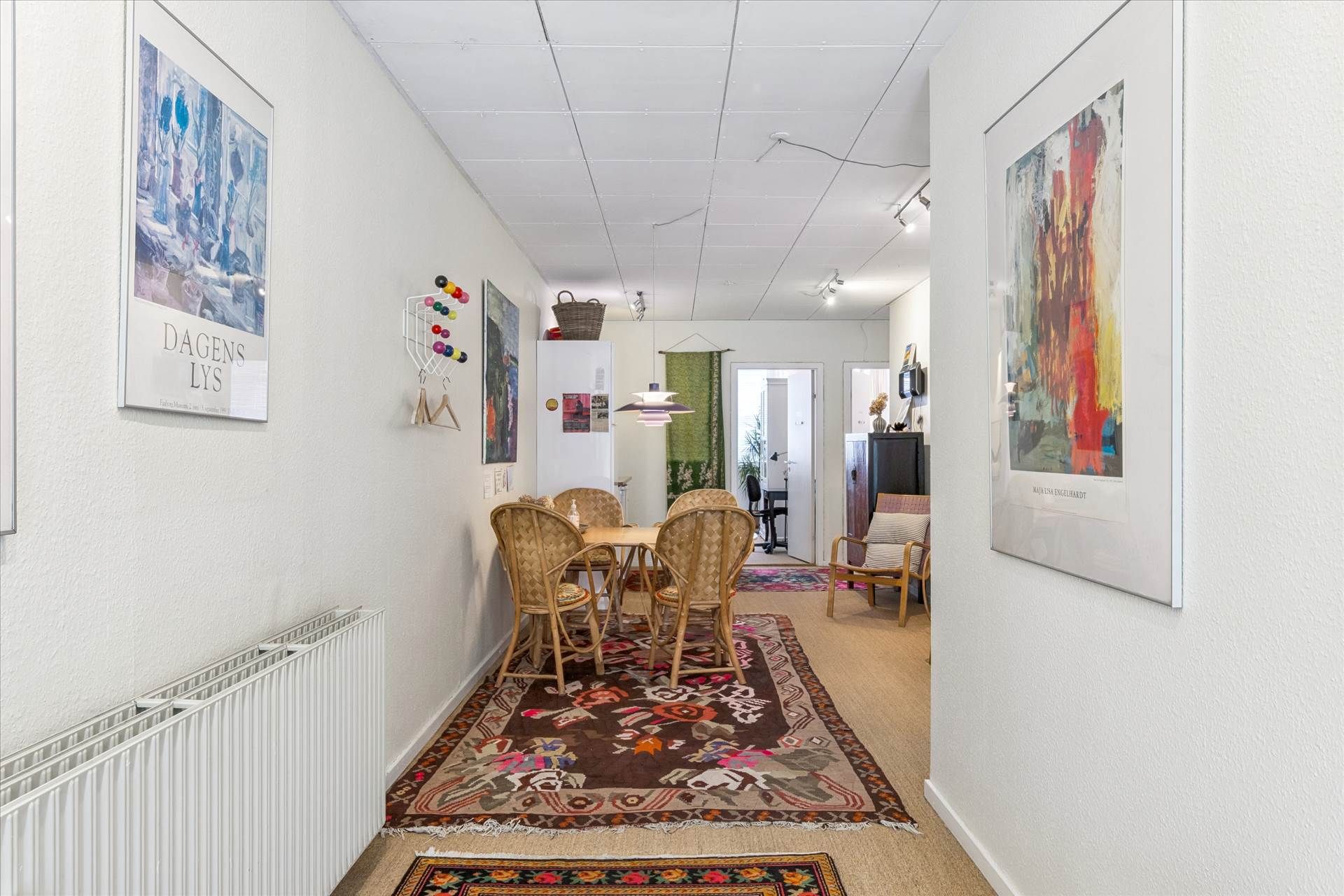 Hvidt vægmaleri med kunstværker og lysekroner på loftet og to smukke gulvtæpper i gangen