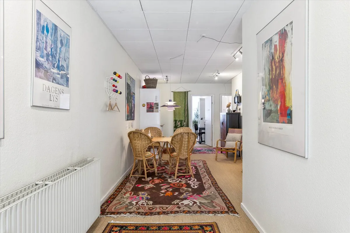 Hvidt vægmaleri med kunstværker og lysekroner på loftet og to smukke gulvtæpper i gangen