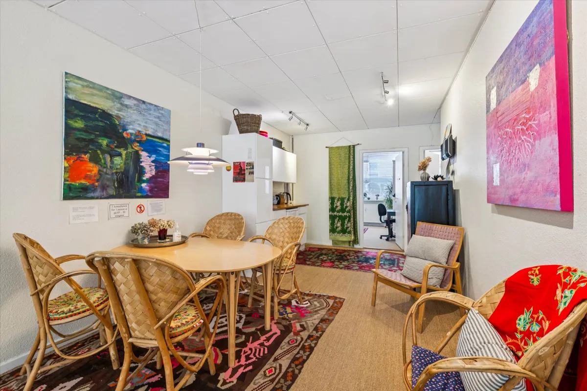 Lys stue med lysegul væg og lysekroner, stole og spisebord samt kunstværker og tæppe på gulvet