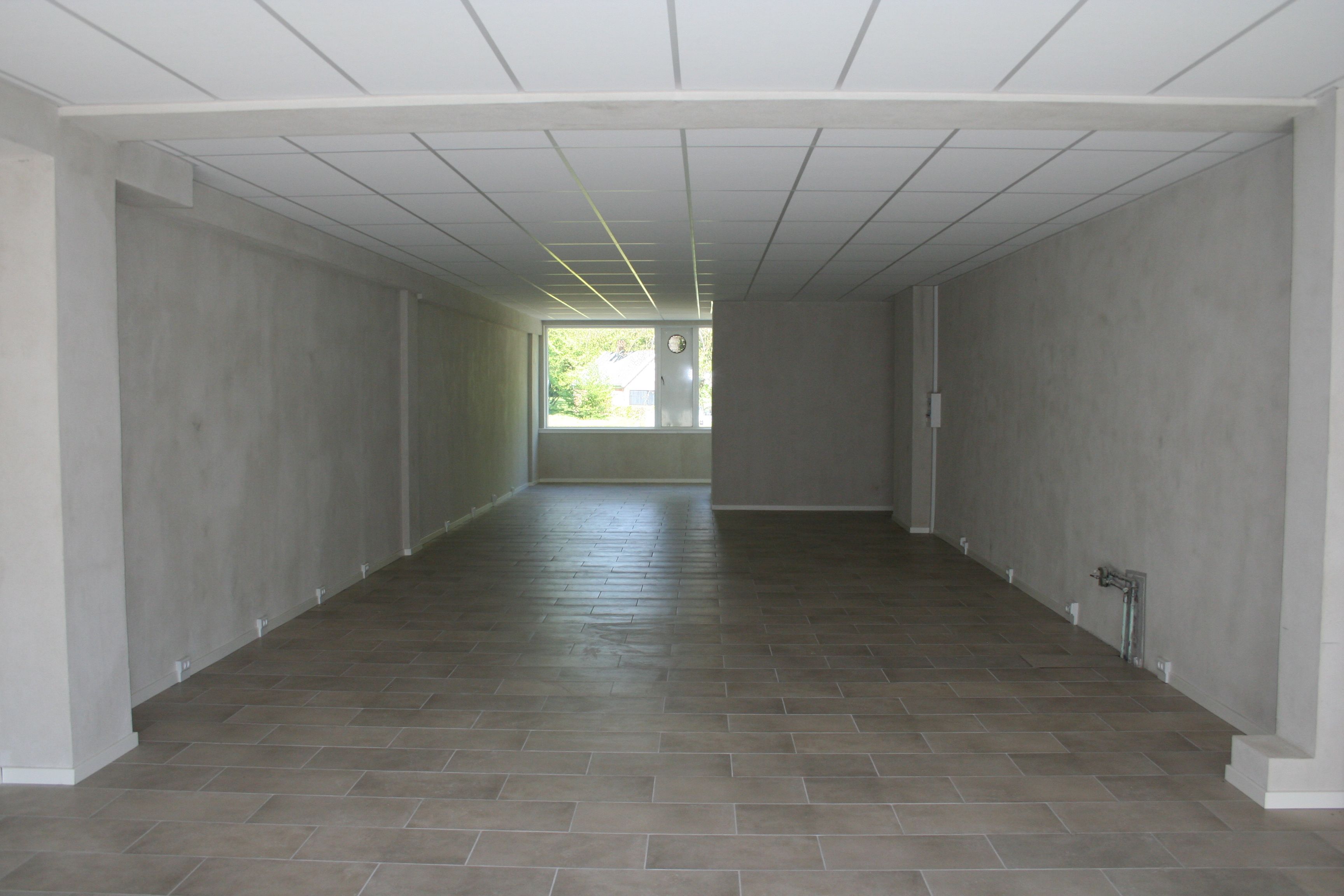 Ledig butikslejemål med store vinduer og glat gulv i moderne interiør med hvidt loft og vægge.