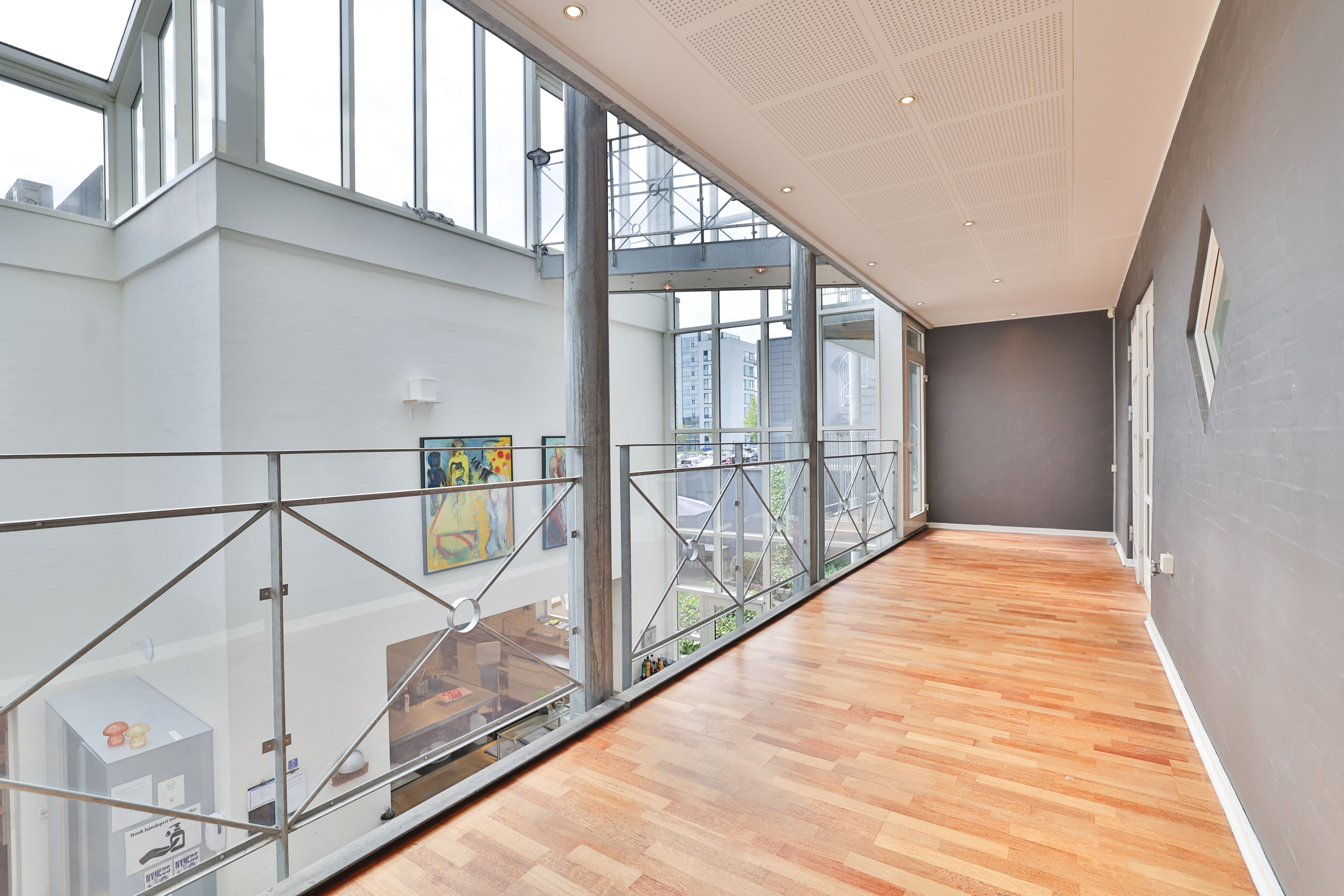 En kontoretræppegang med glasvinduer og metalværker, lyse lofter og trægulve samt vægmalerier og en moderne indretning