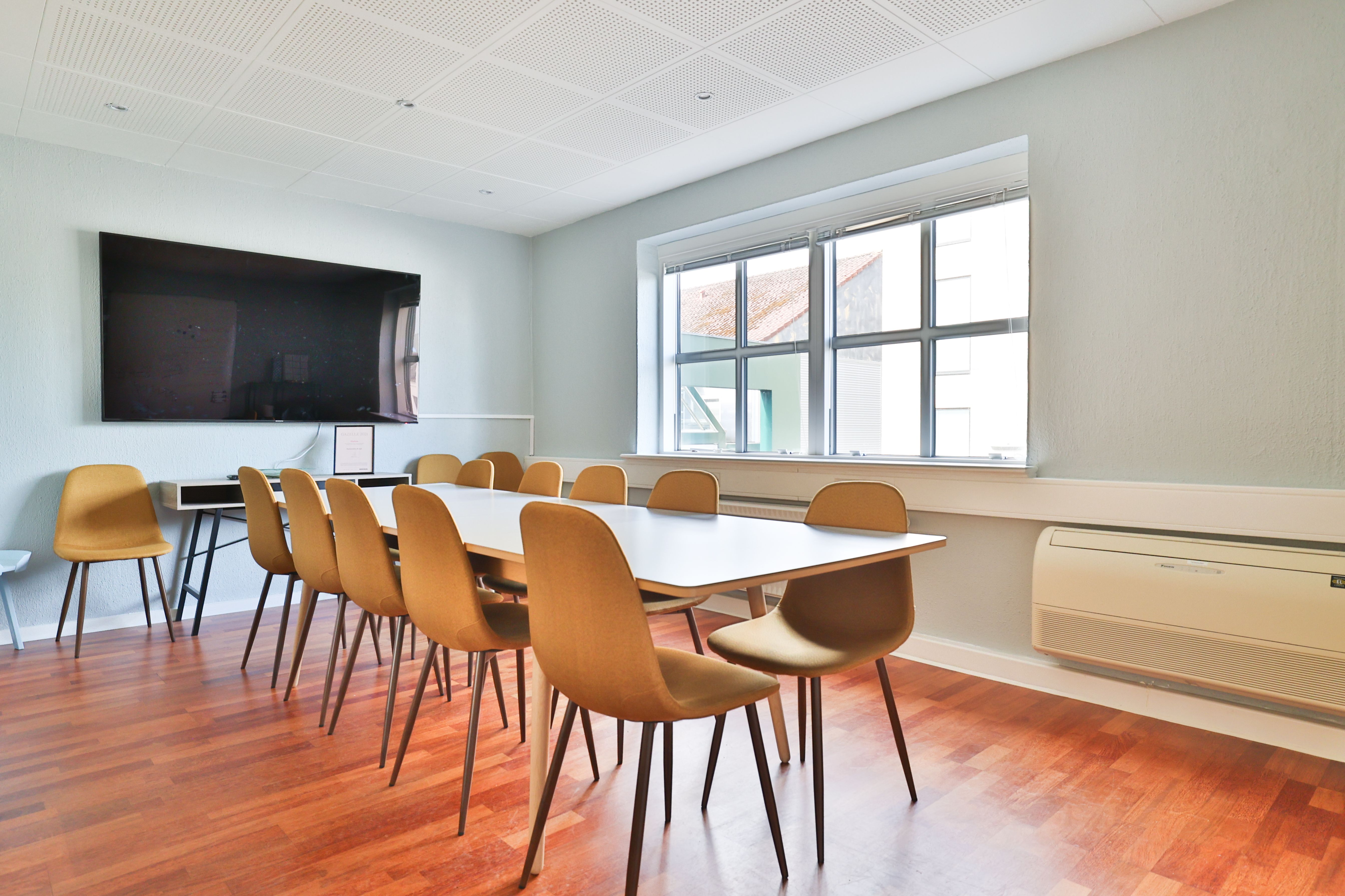 Lyst kontor med gul stol, hvidt bord, gulv, tv og klimaanlæg ved vinduet