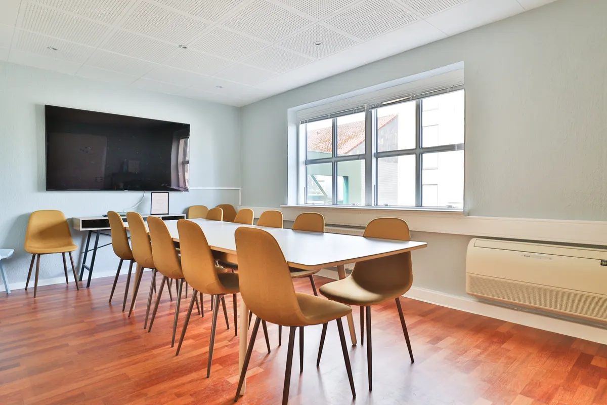 Lyst kontor med gul stol, hvidt bord, gulv, tv og klimaanlæg ved vinduet