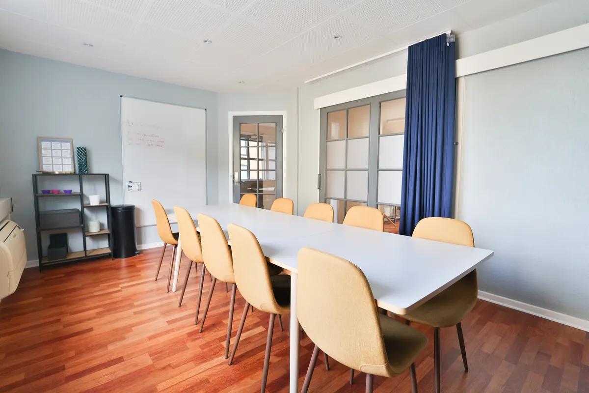 En stor møde- og konferencesal med et langt hvidt bord og lyse gule stole. Et whiteboard og en sort skraldspande står på den