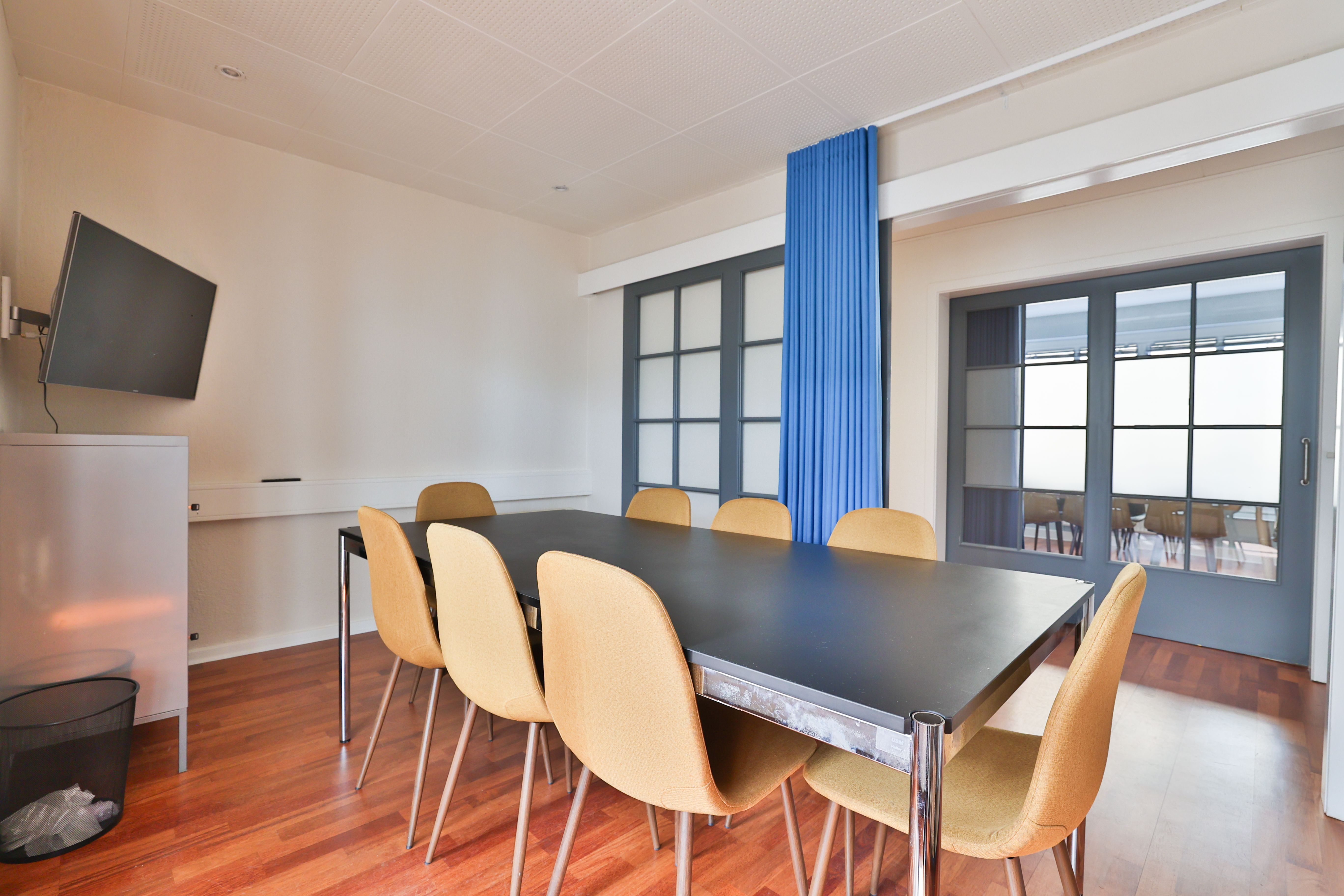 Kontor med en stor bord og fire stol og en tv-skærm og smukke vinduer med gardiner og en skraldspande