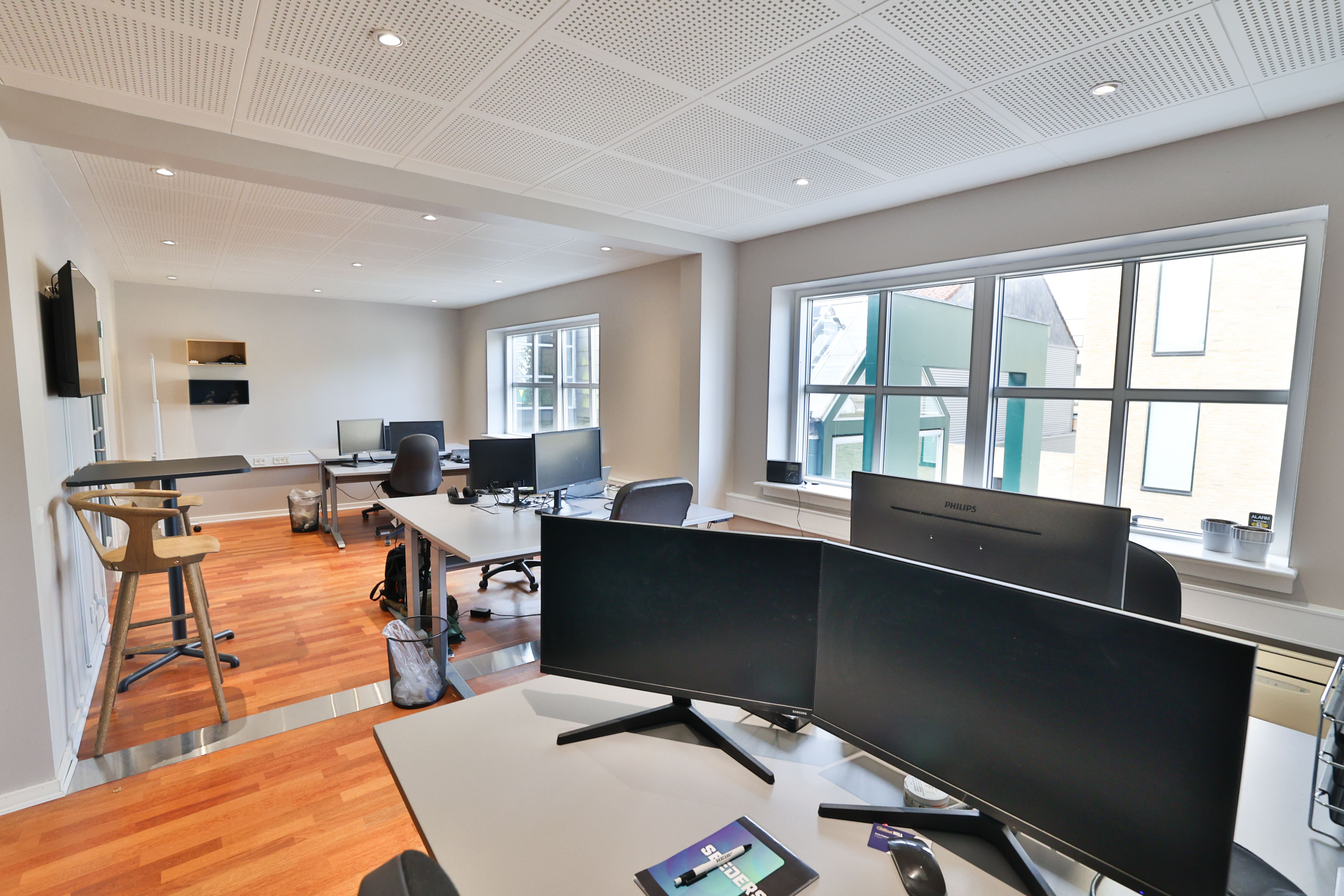 Kontor med trægulv, lyse lofter og skriveborde med Philips-skærme, stol og bokse på gulvet