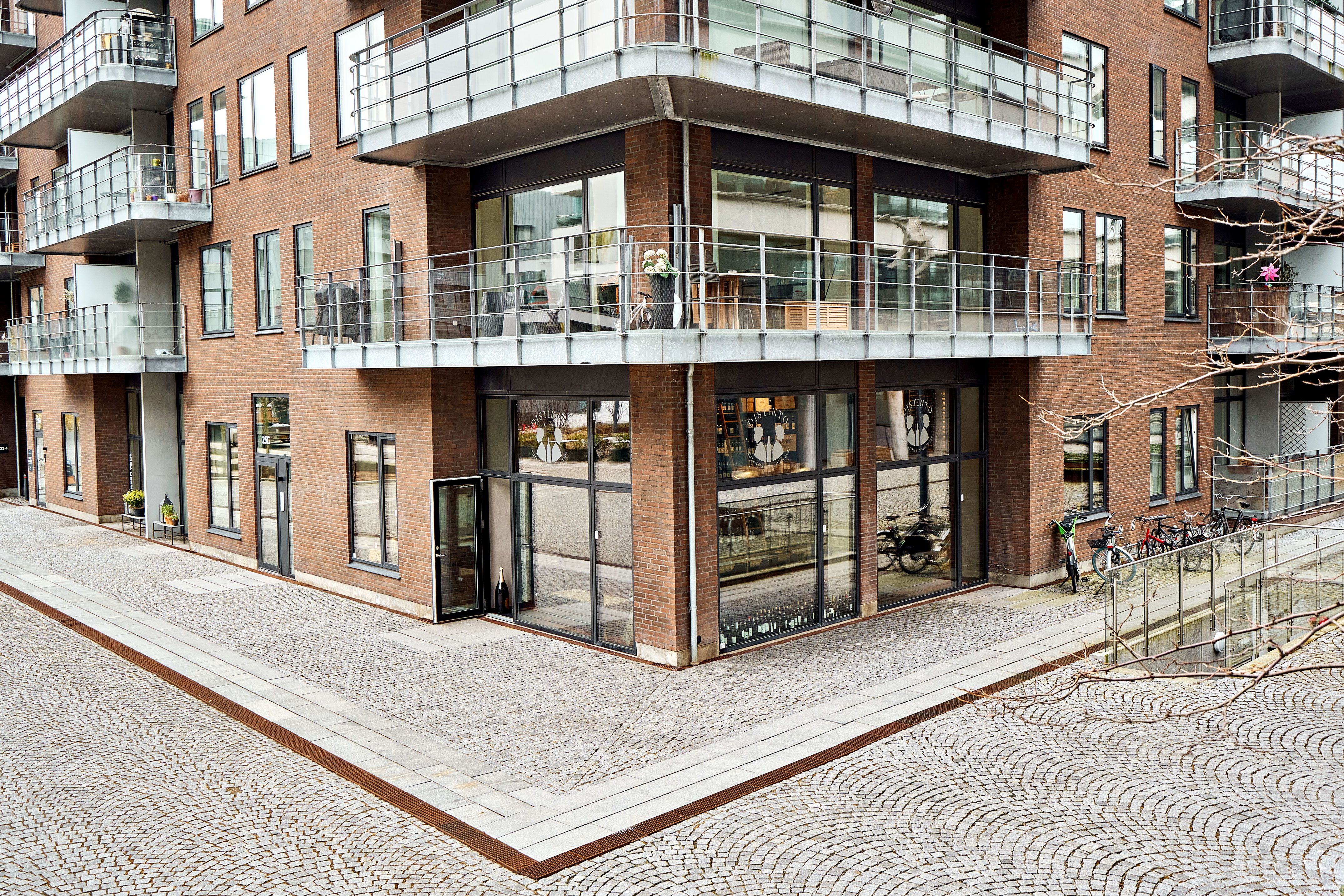 Moderne bygning med terrasse, store glasruder og balkoner i København. En cykelparkering og terrasse med blomster og en