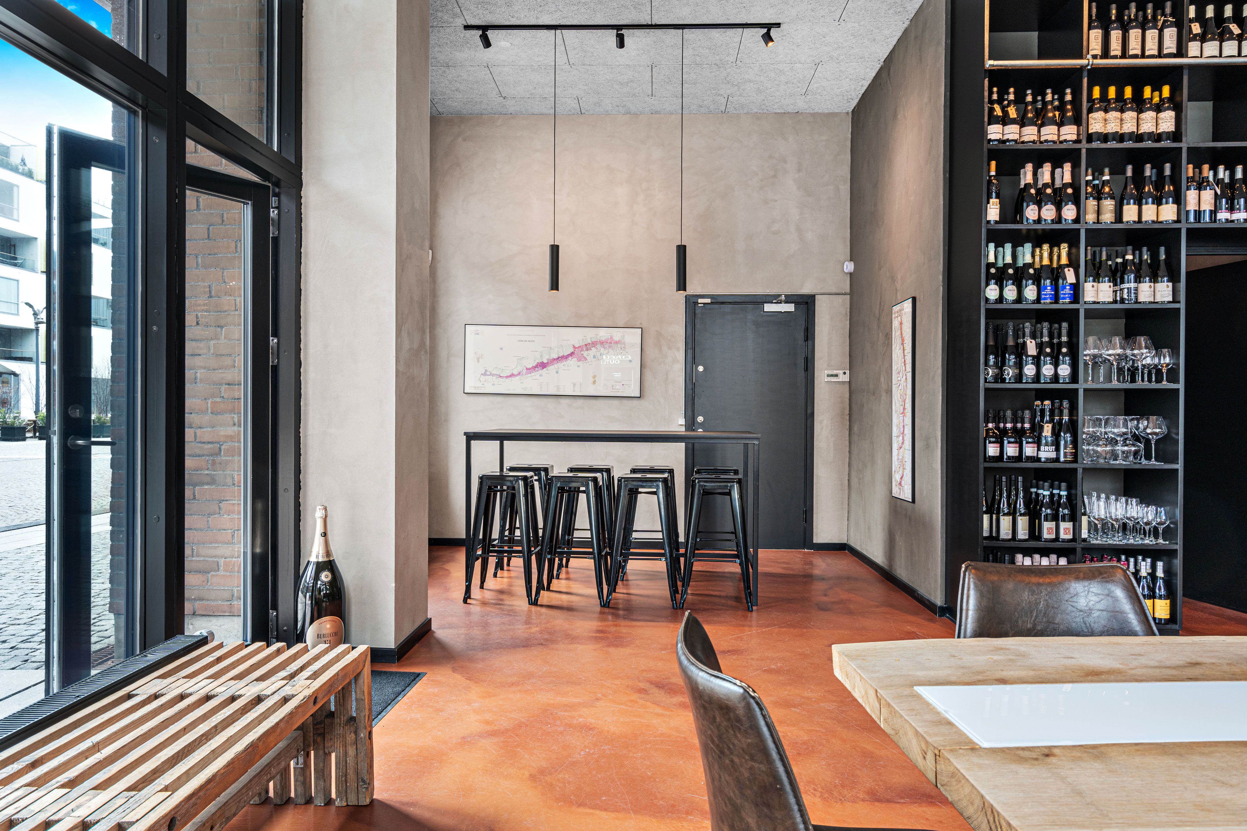 Indenfor et moderne interiør med røde gulvbelægning og høje vinduer er der et bord med stole, og læderstole ved et bord og