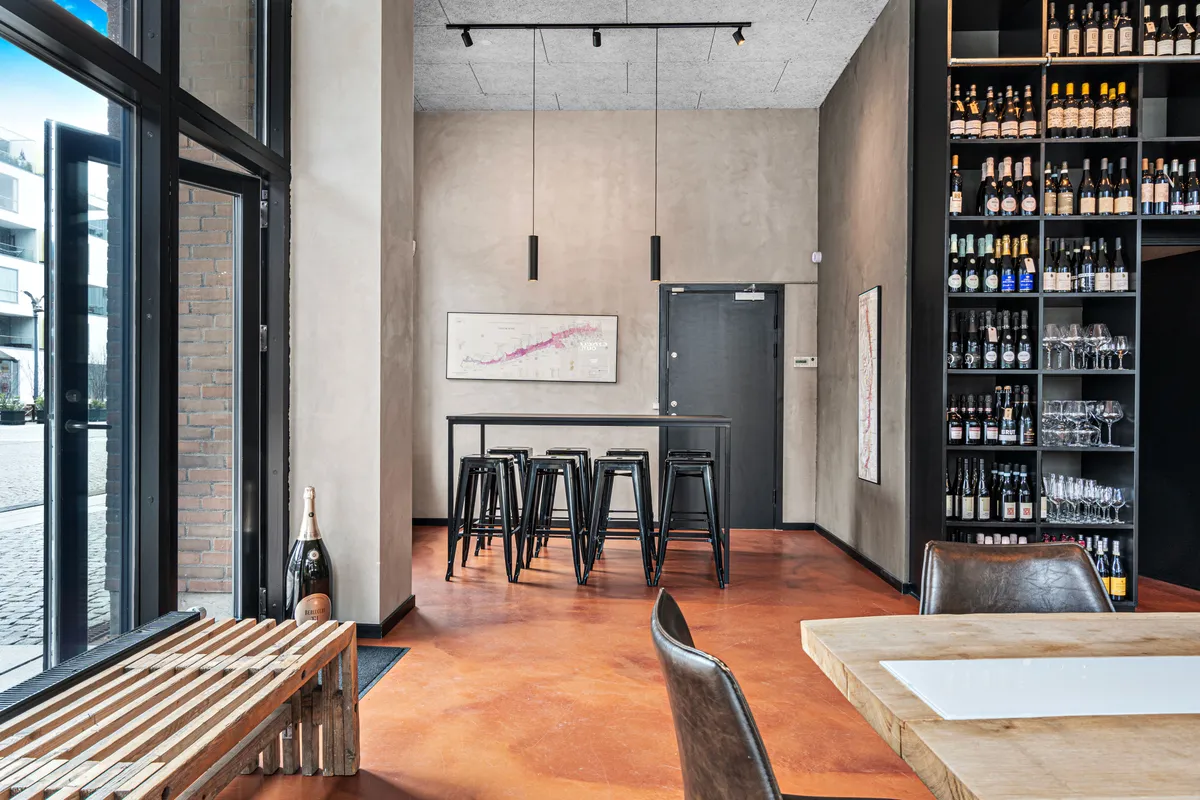 Indenfor et moderne interiør med røde gulvbelægning og høje vinduer er der et bord med stole, og læderstole ved et bord og