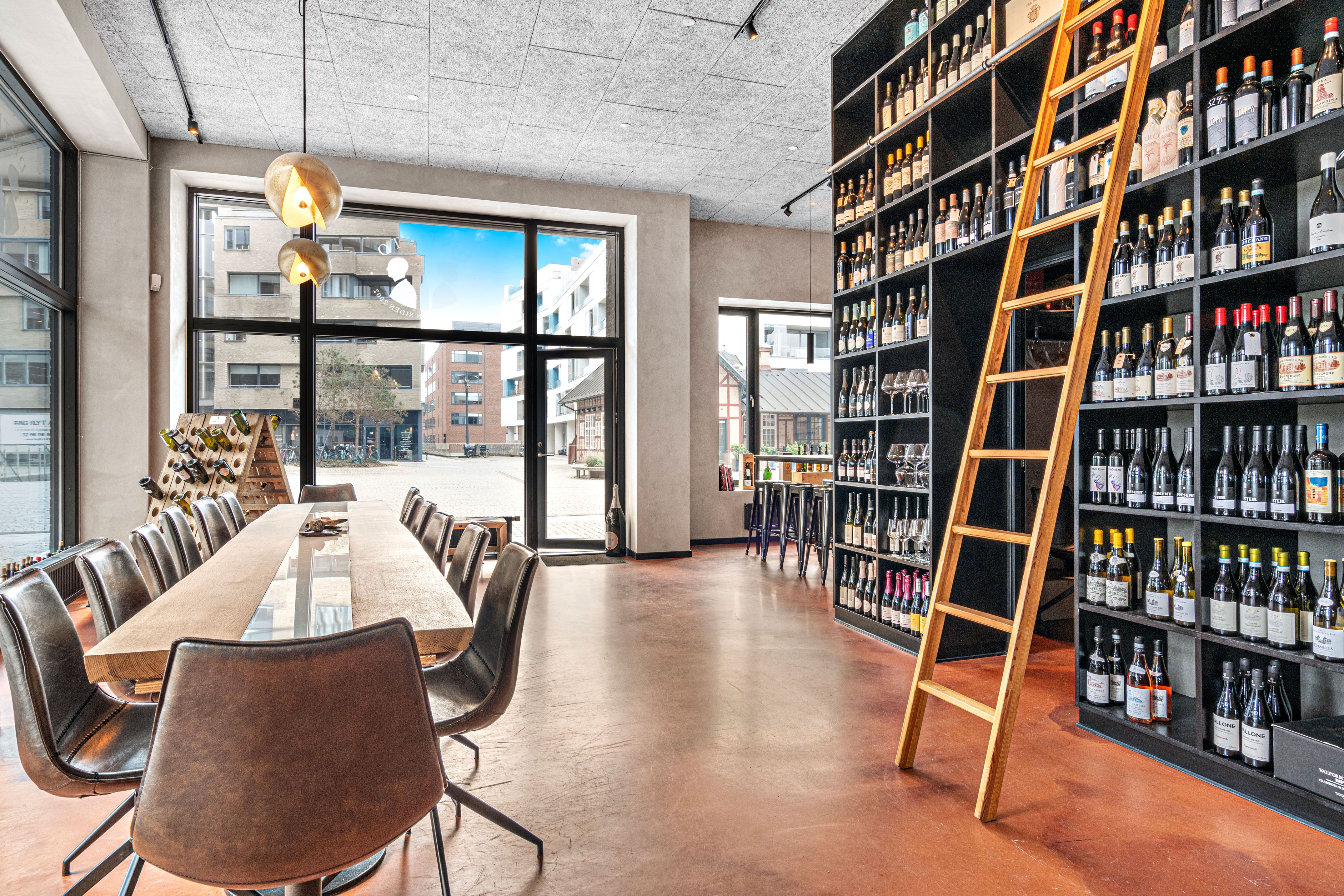 Værelse med læderstole og langt bord, vinflasker og vinduer med udsigt til byen og park