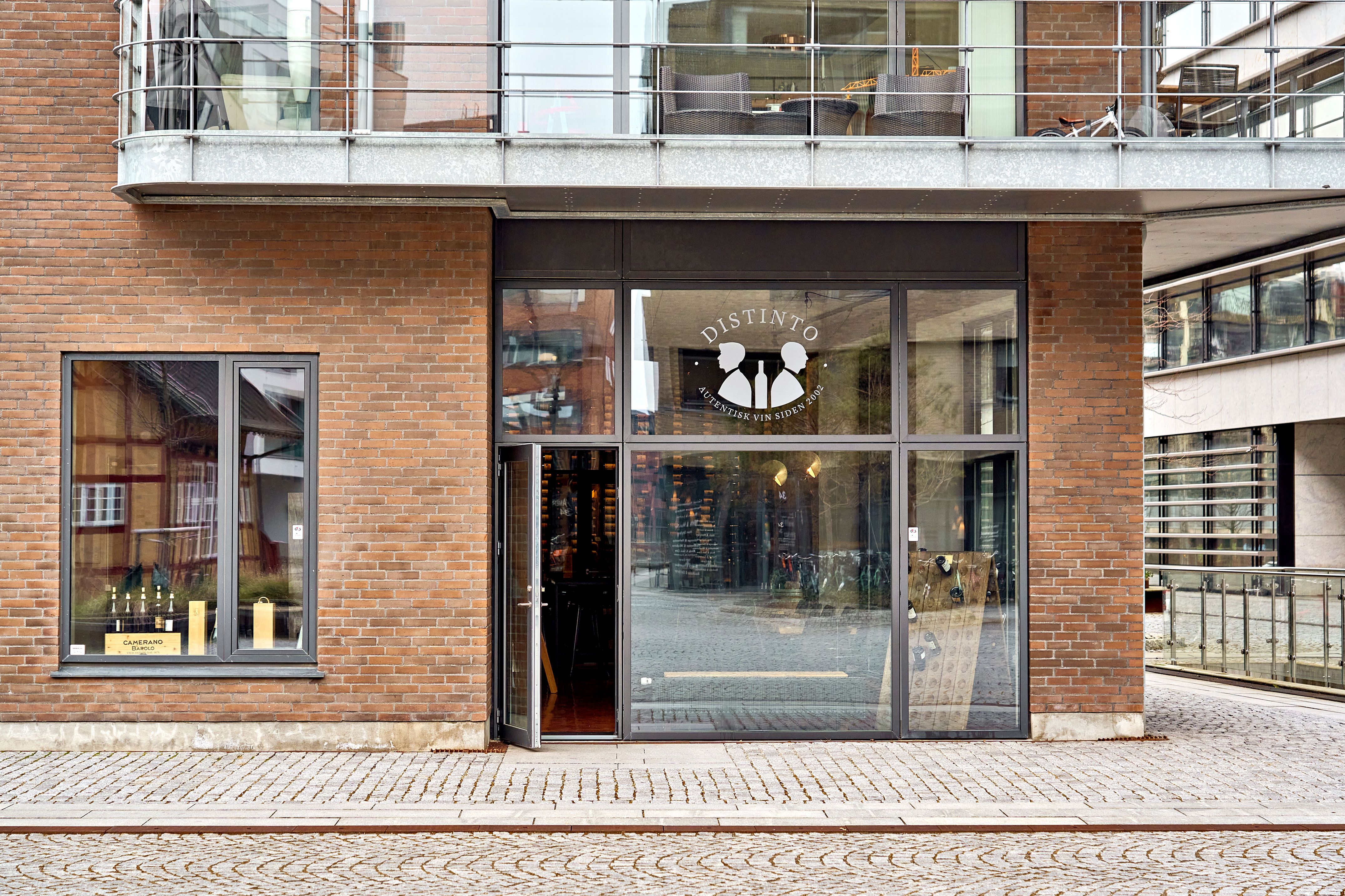 En vinbutik med navnet Distinto, der er placeret i en bygning med røde mursten og glasvinduer og døre, der vender ud mod en