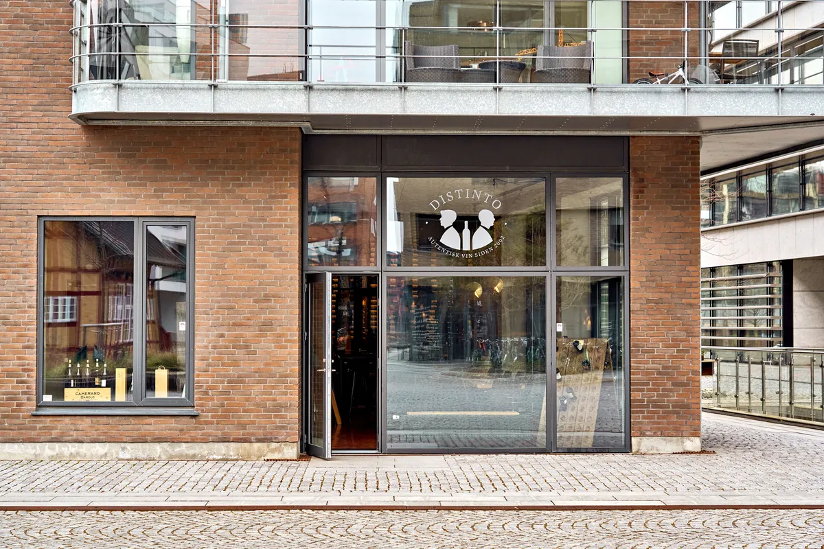 En vinbutik med navnet Distinto, der er placeret i en bygning med røde mursten og glasvinduer og døre, der vender ud mod en