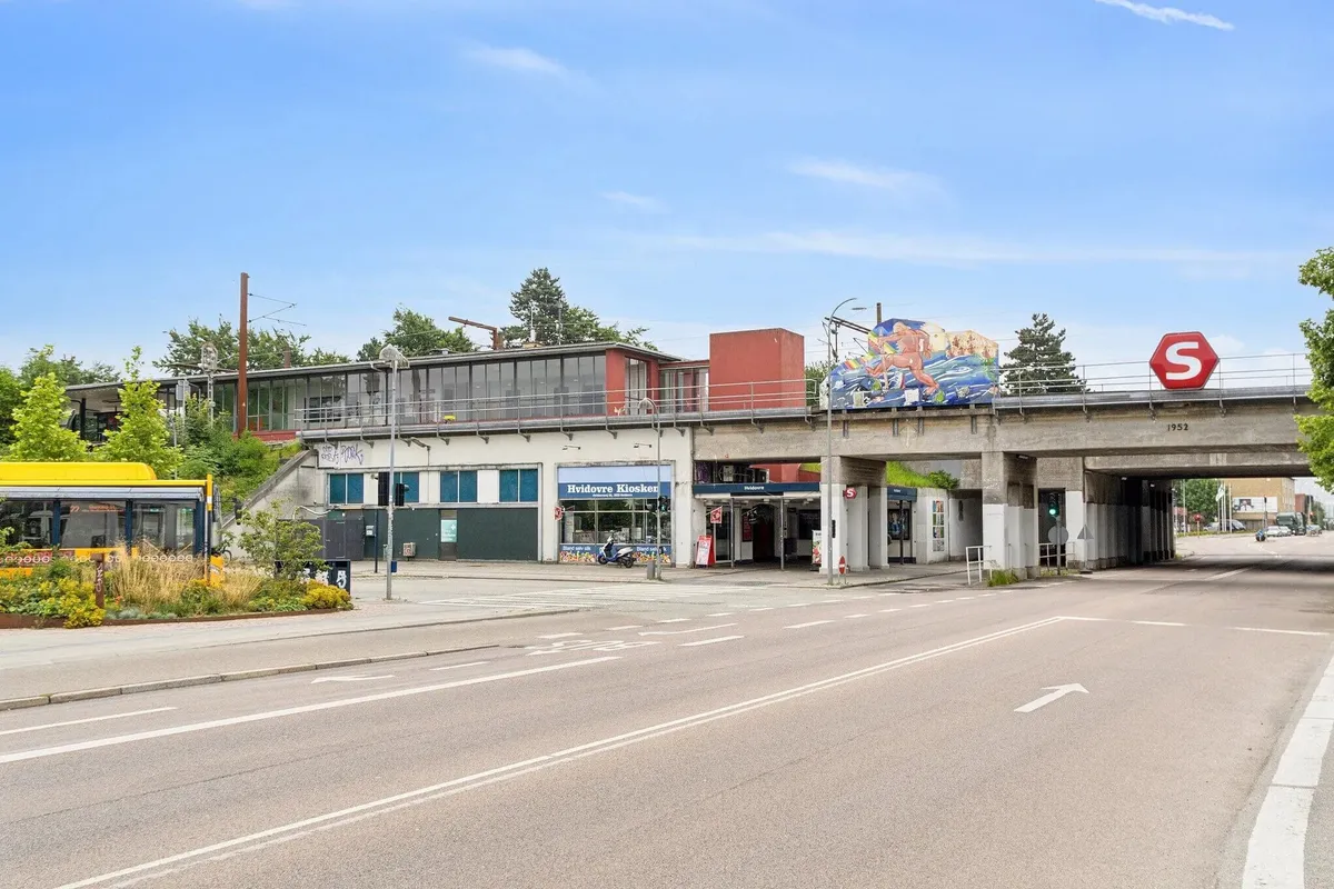 En vejkryds med stopskilt og en overgang for gående og cyklister, parkeret bus og grønne planter i forgrunden