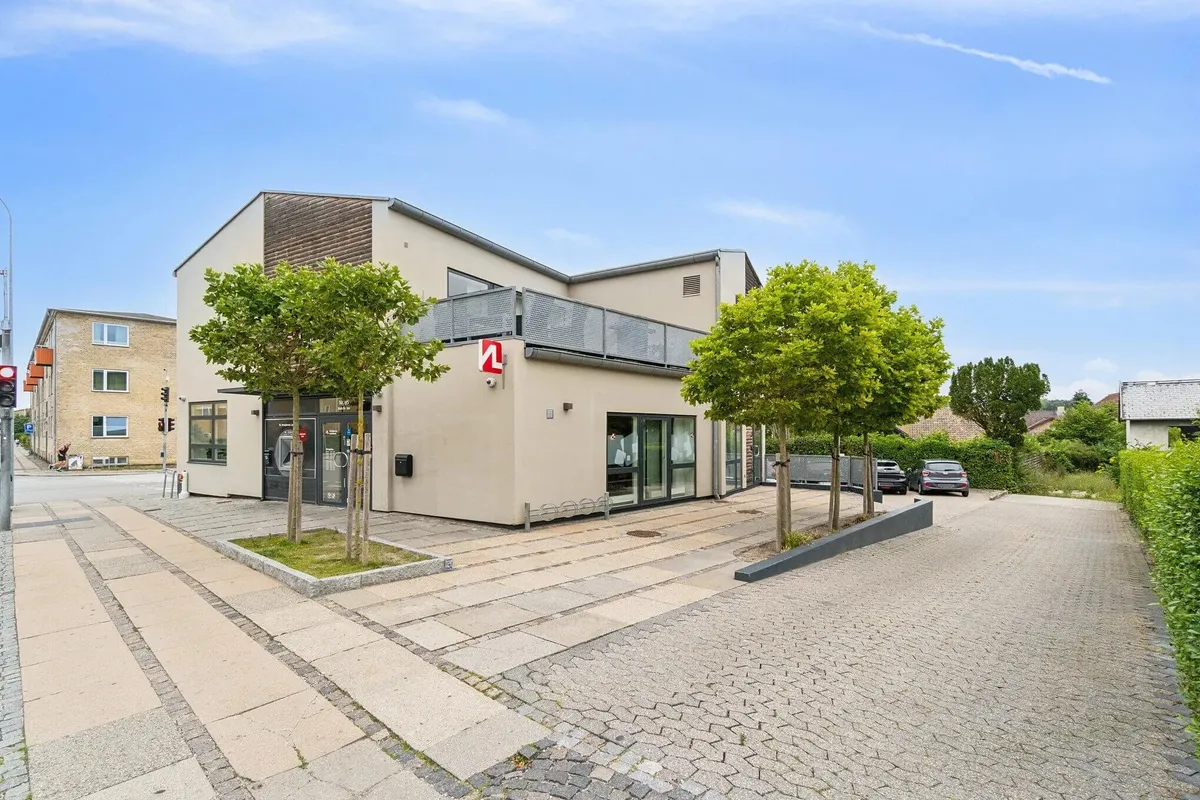 Et velholdt erhvervslokal med let at læse rødt N og gule skilte på facaden, parkeringsplads og to biler foran bygningen