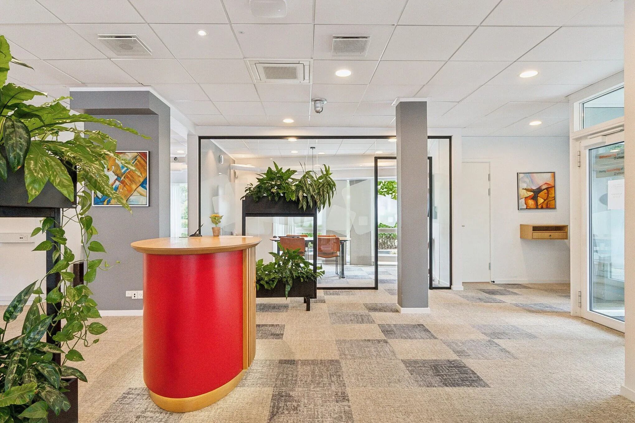 Modernt mødelokale med lyse møbler og store vinduer samt kunstværker på væggene